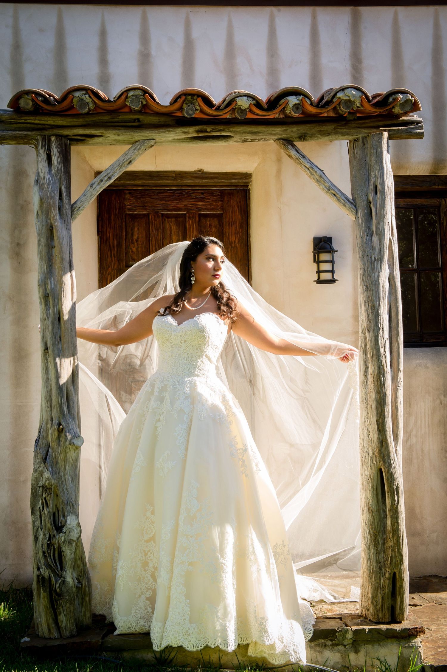 Bride in flowing white dress poses dramatically in front of Spanish colonial architecture.