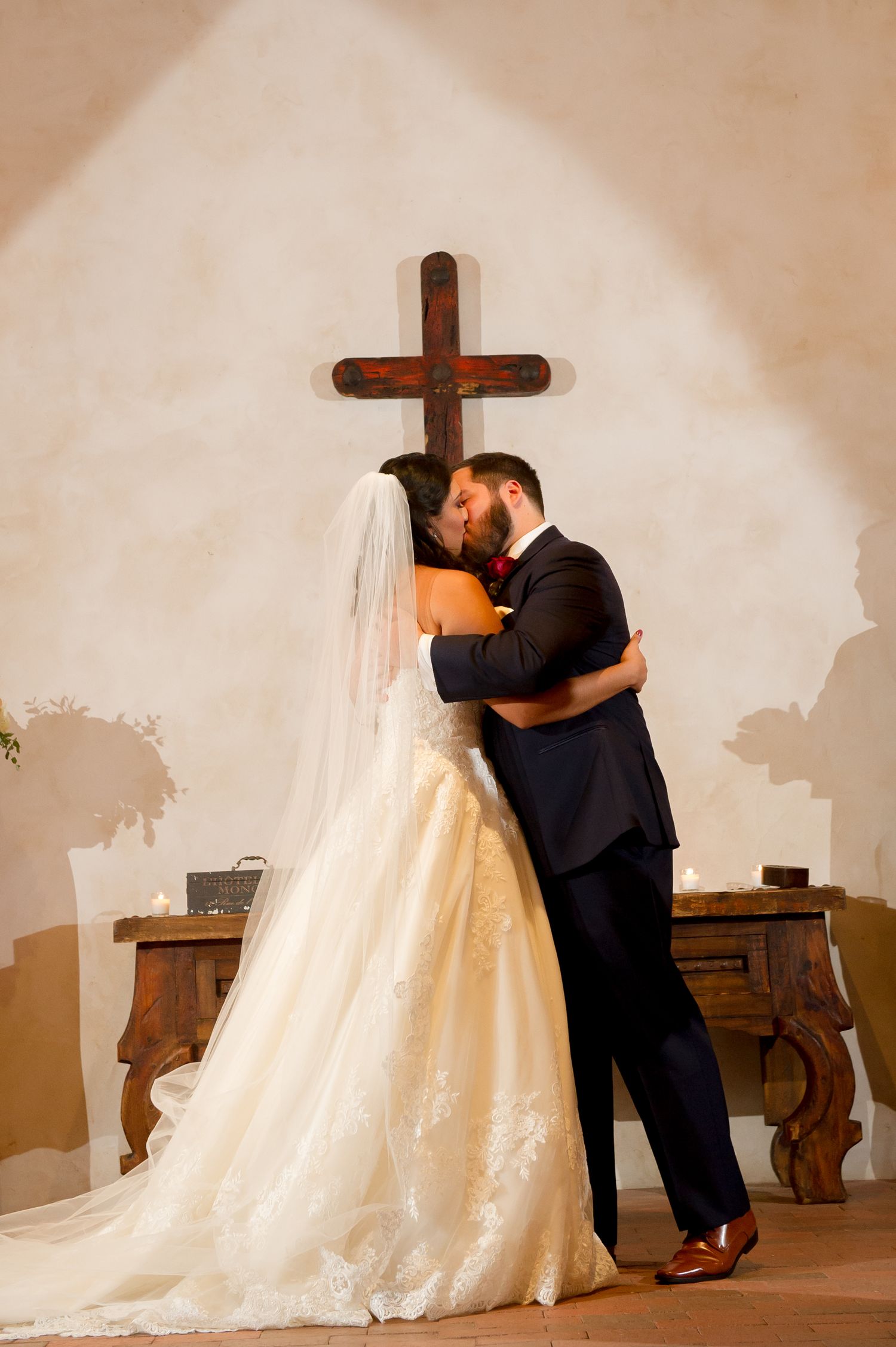 A couple shares their first kiss as newlyweds in front of a wooden cross at their church wedding.
