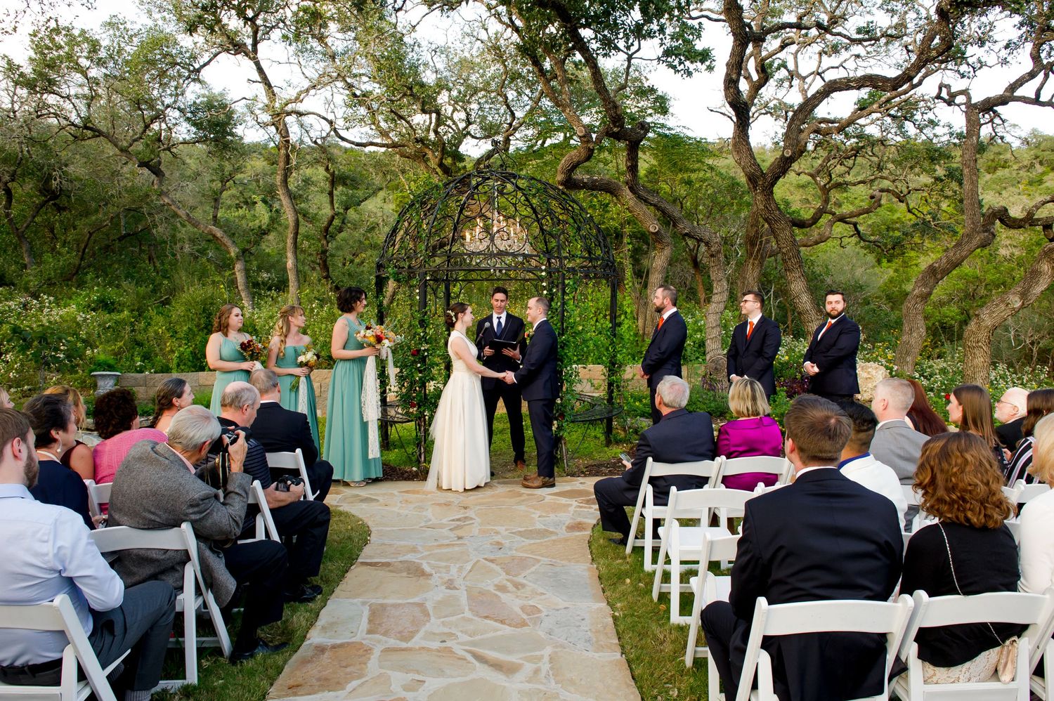 Outdoor wedding ceremony setup with white chairs and stone pathway surrounded by lush greenery.