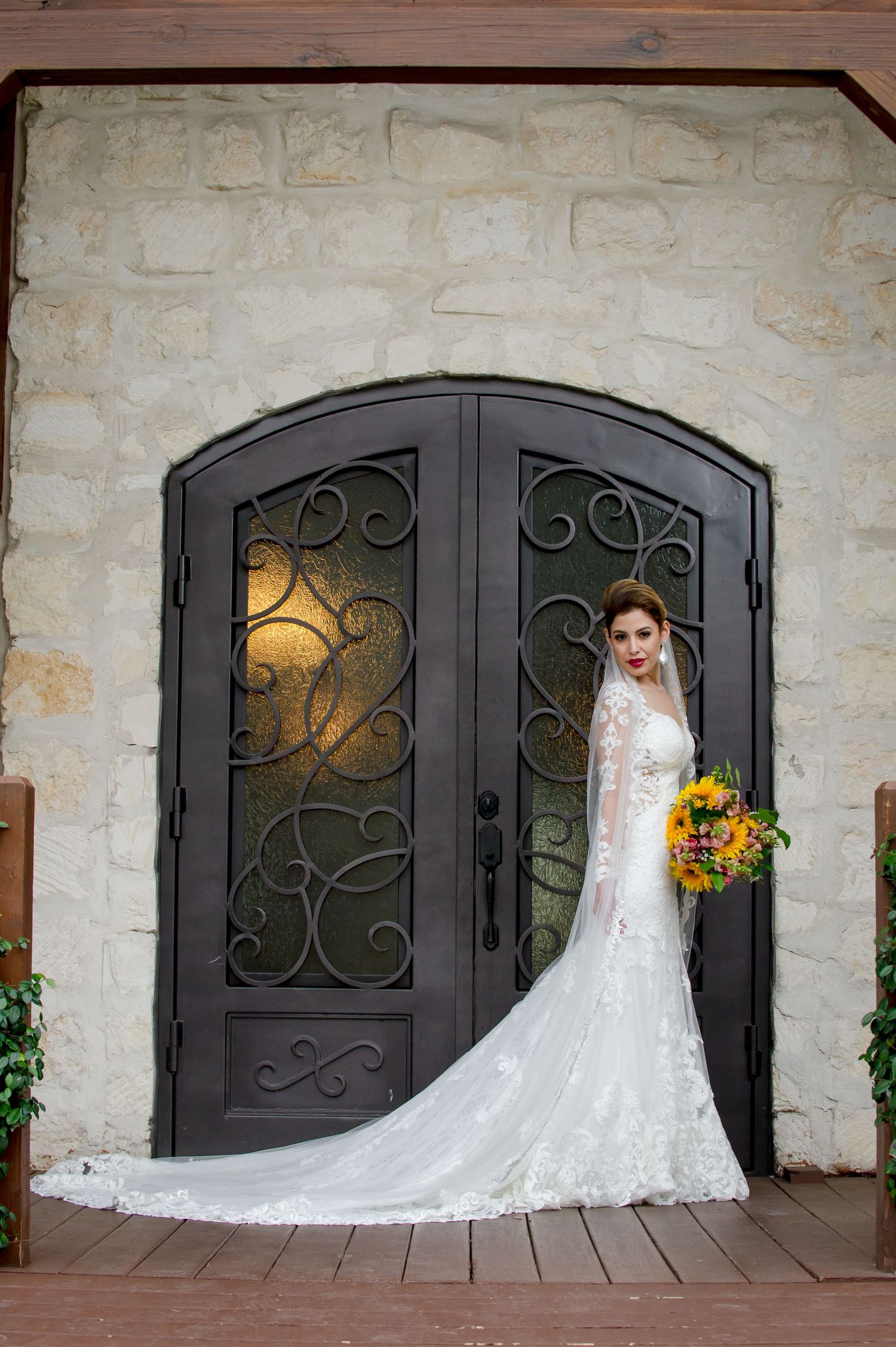 Wedding dress train spreads elegantly across stone floor in front of ornate iron doors.