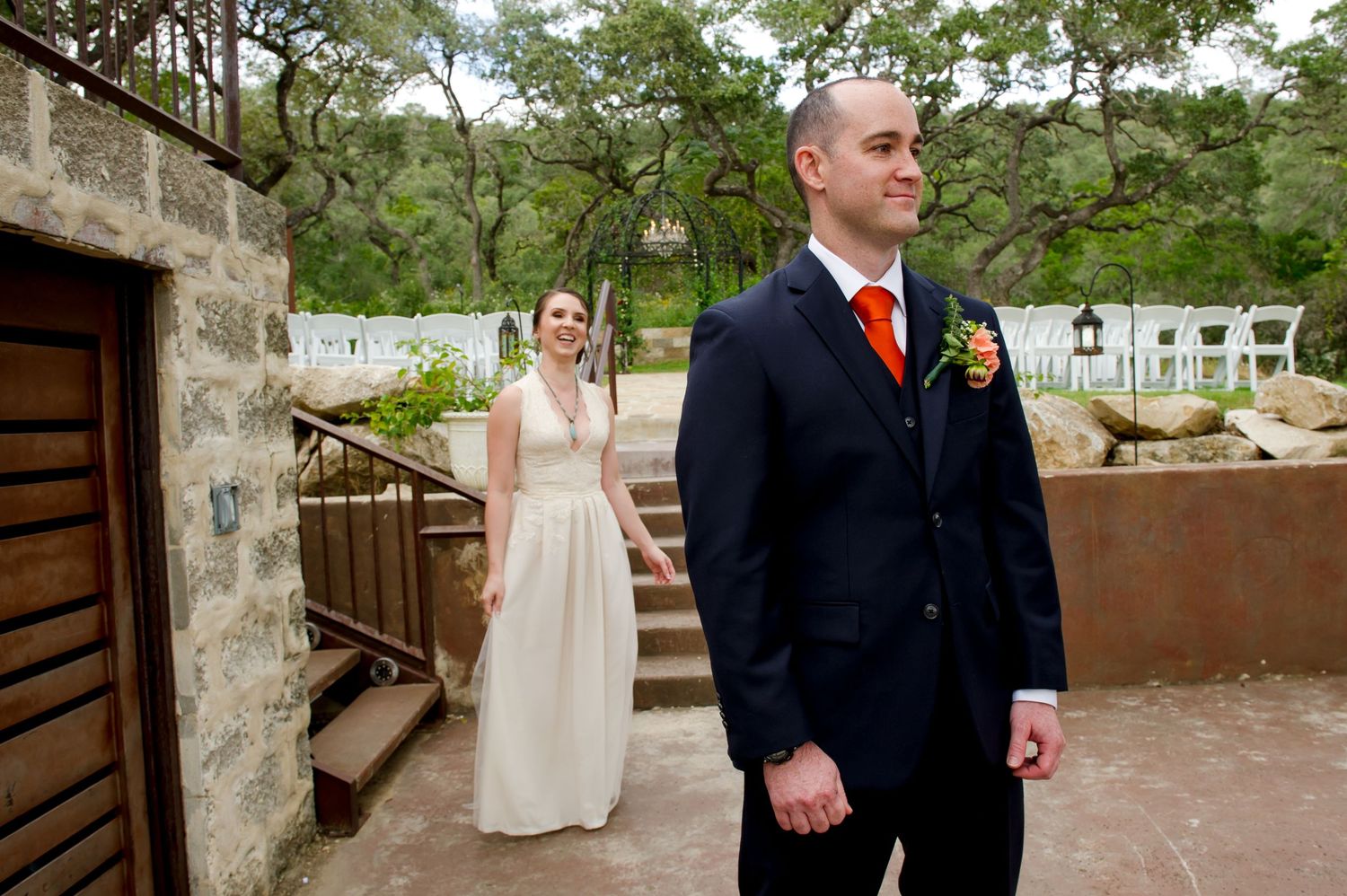 A wedding couple stands in front of rustic stone walls and greenery during an outdoor ceremony.