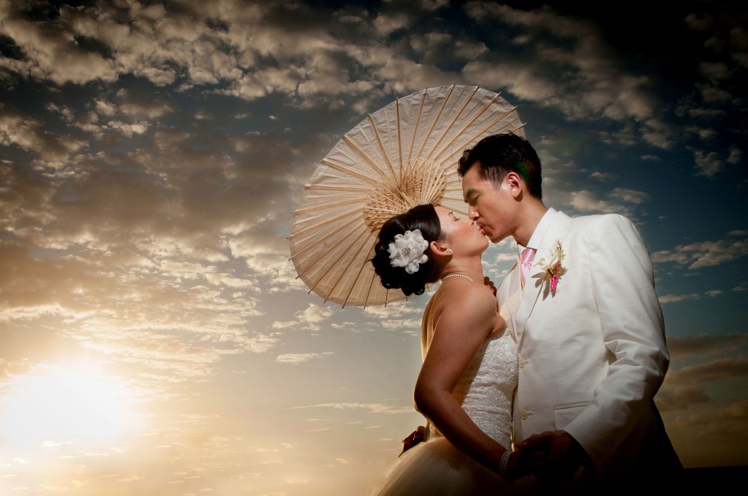 Romantic sunset wedding photos with decorative parasol against cloudy sky.