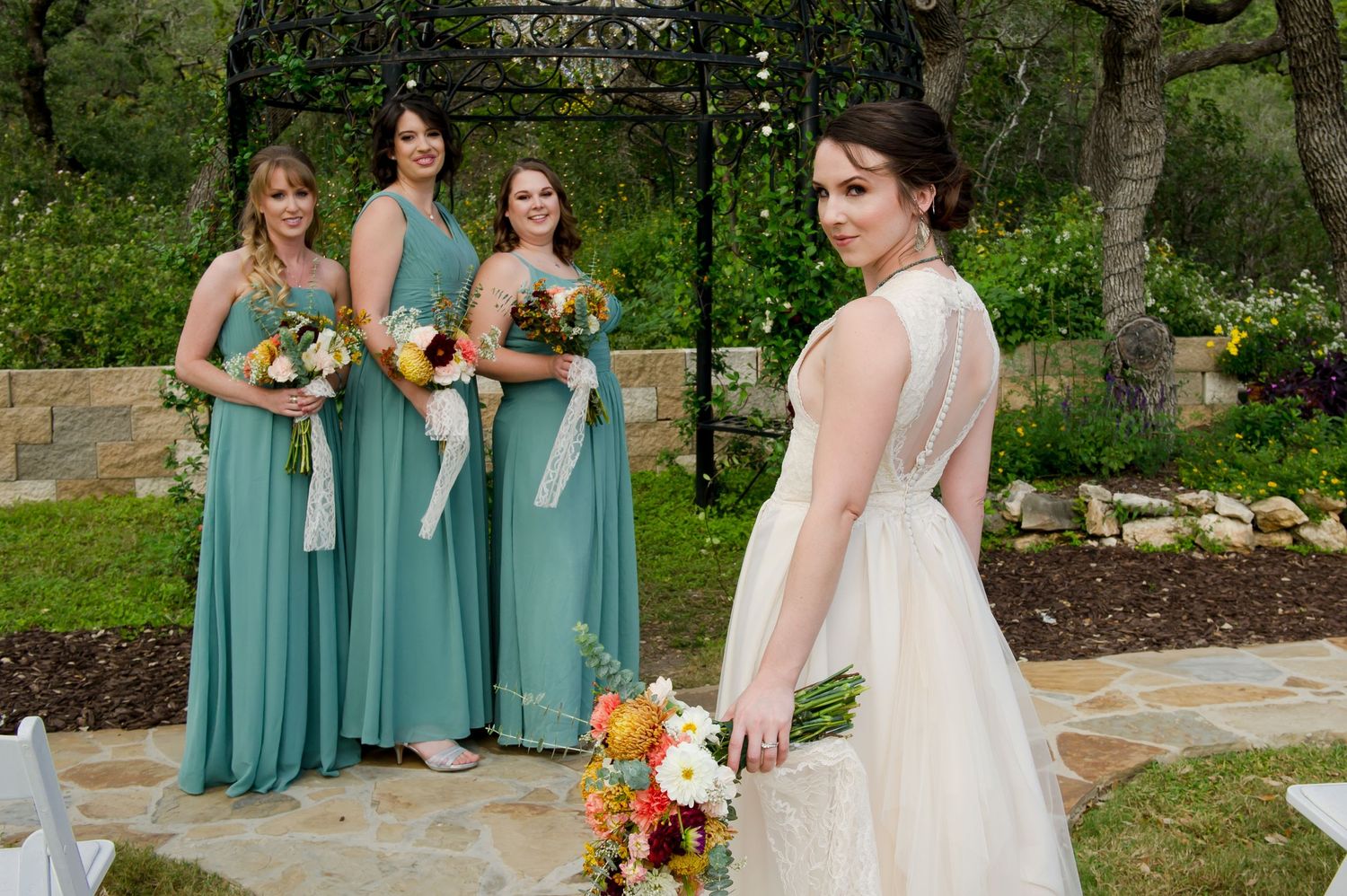Wedding party in seafoam green bridesmaid dresses posing together outdoors in a garden setting.