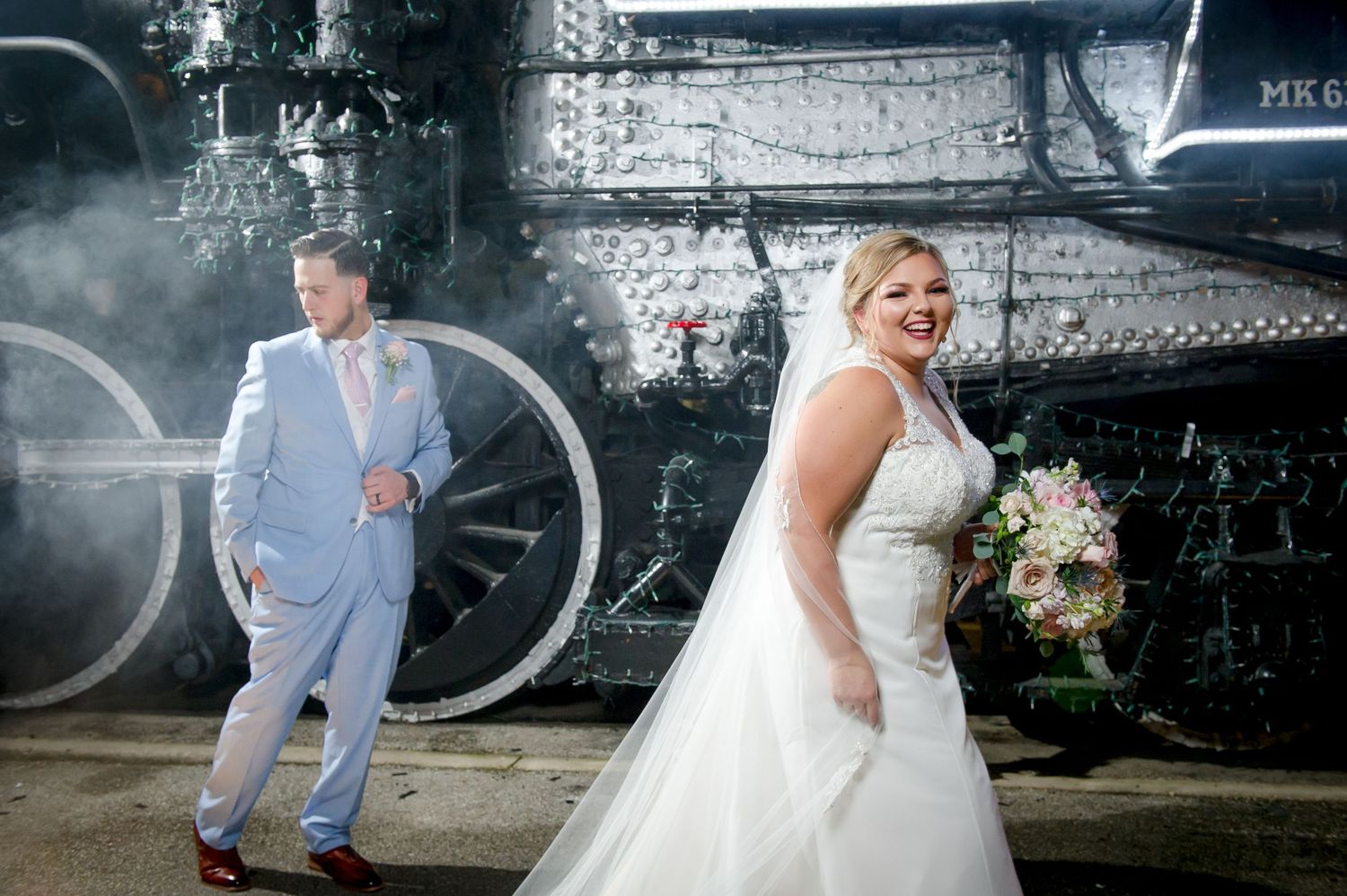 Wedding couple poses dramatically by historic train with flowing white dress.