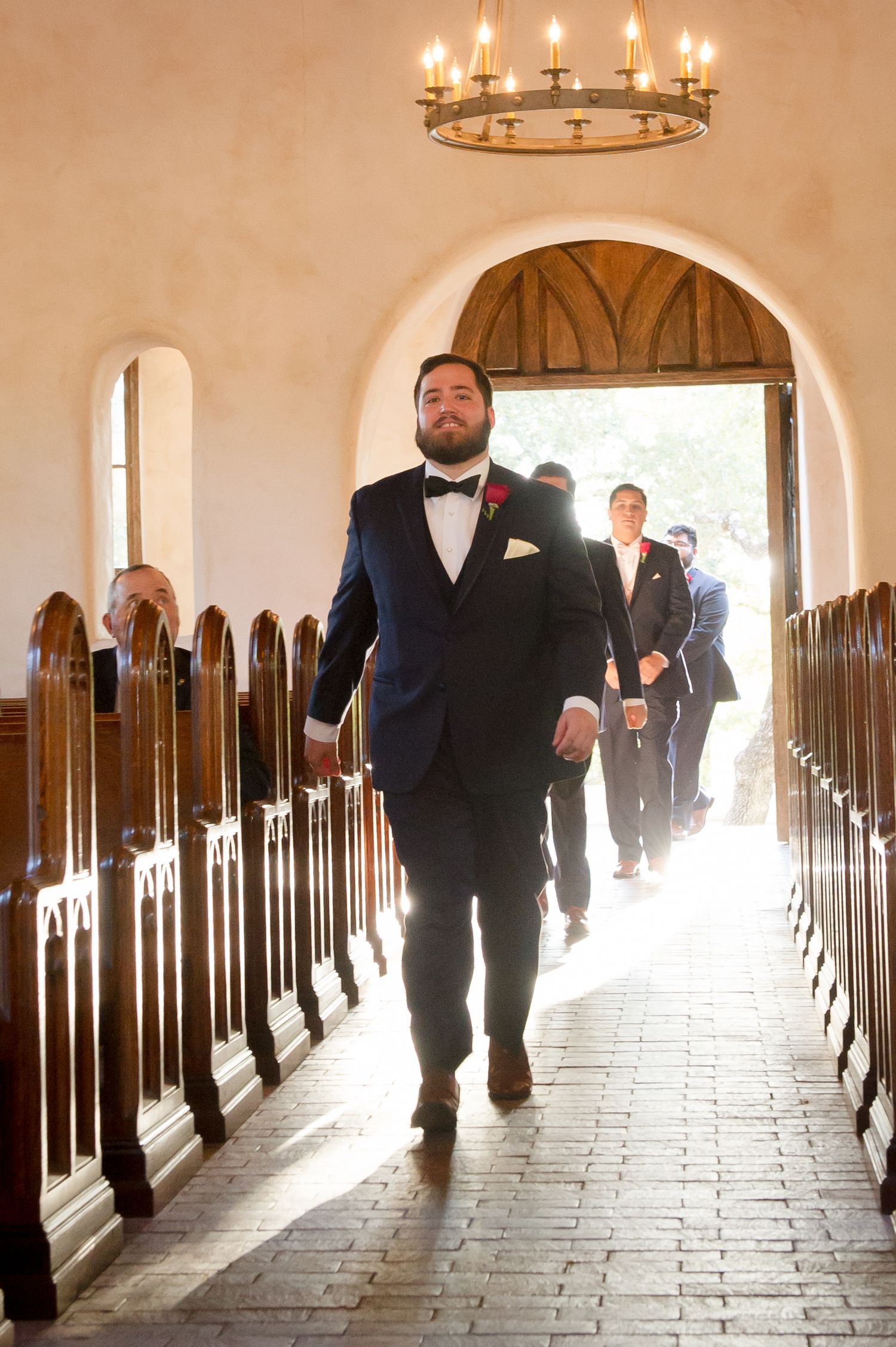A church corridor with wooden pews and chandelier lighting creates a dramatic wedding ceremony setting.