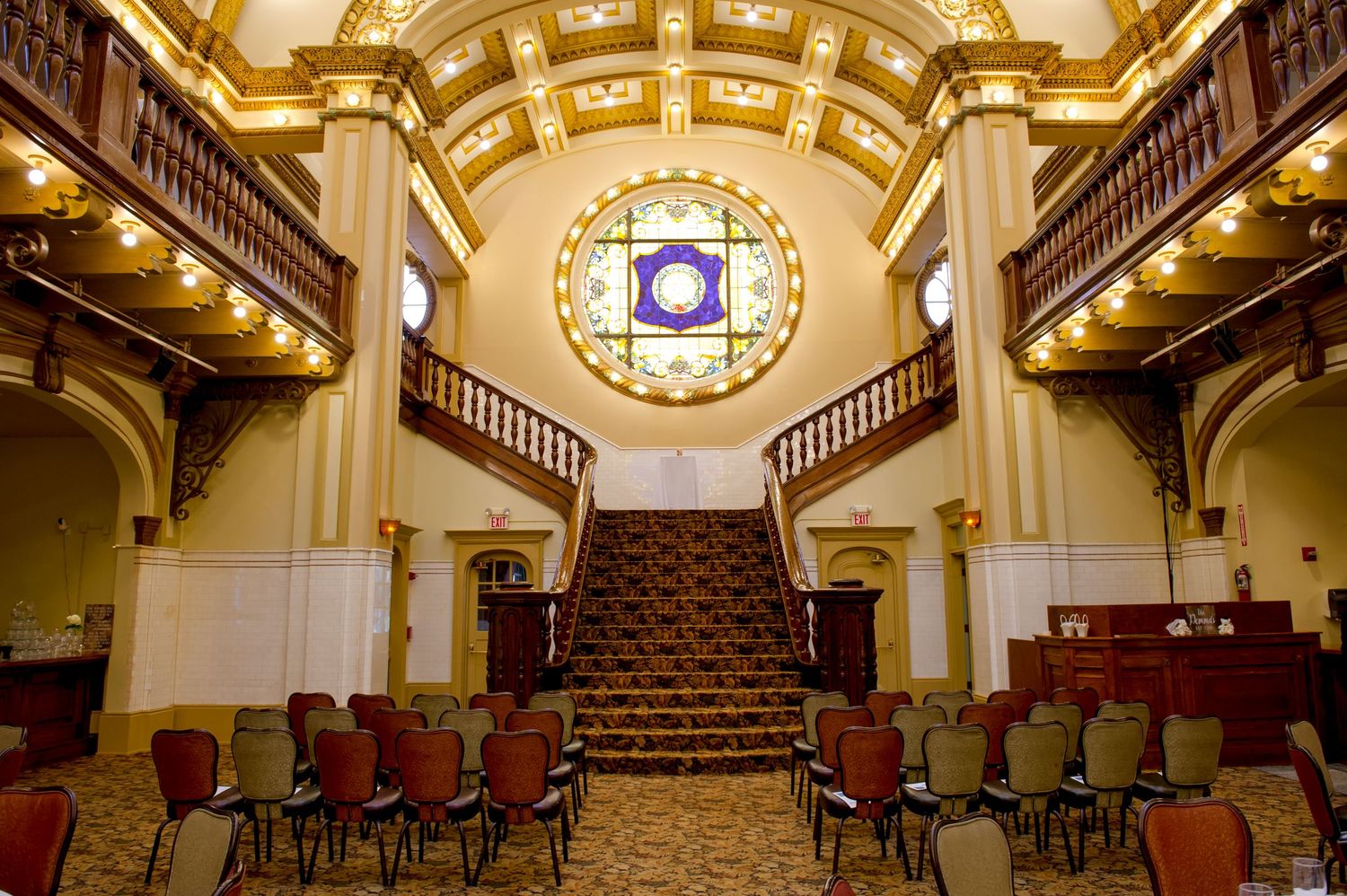 Elegant ballroom with ornate ceiling, wooden railings and theater-style seating.