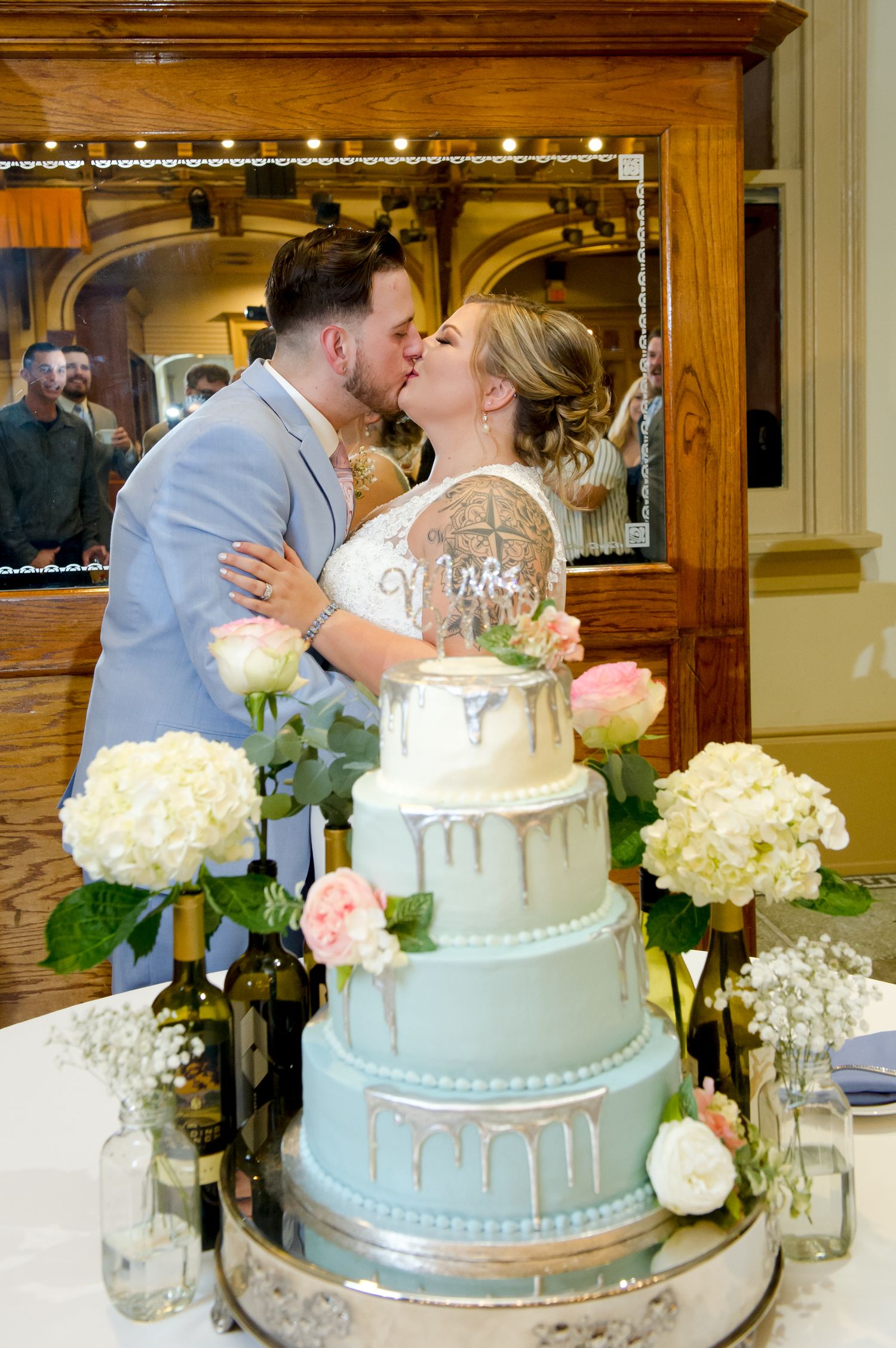Newlyweds share a kiss behind their elegant blue and silver drip wedding cake.