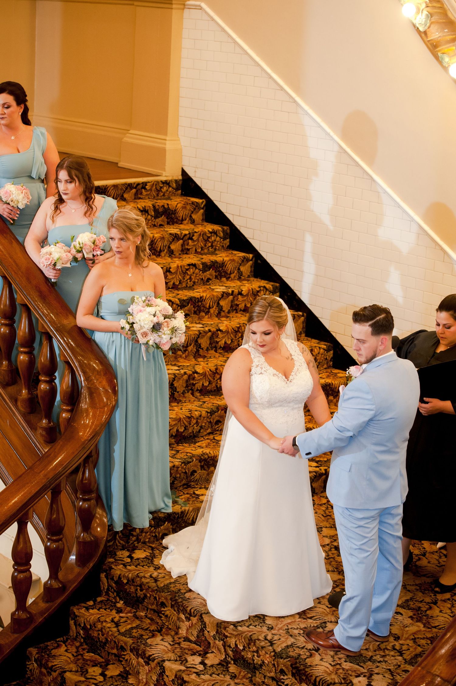 A wedding ceremony moment on an elegant staircase with floral carpeting and wooden banisters.