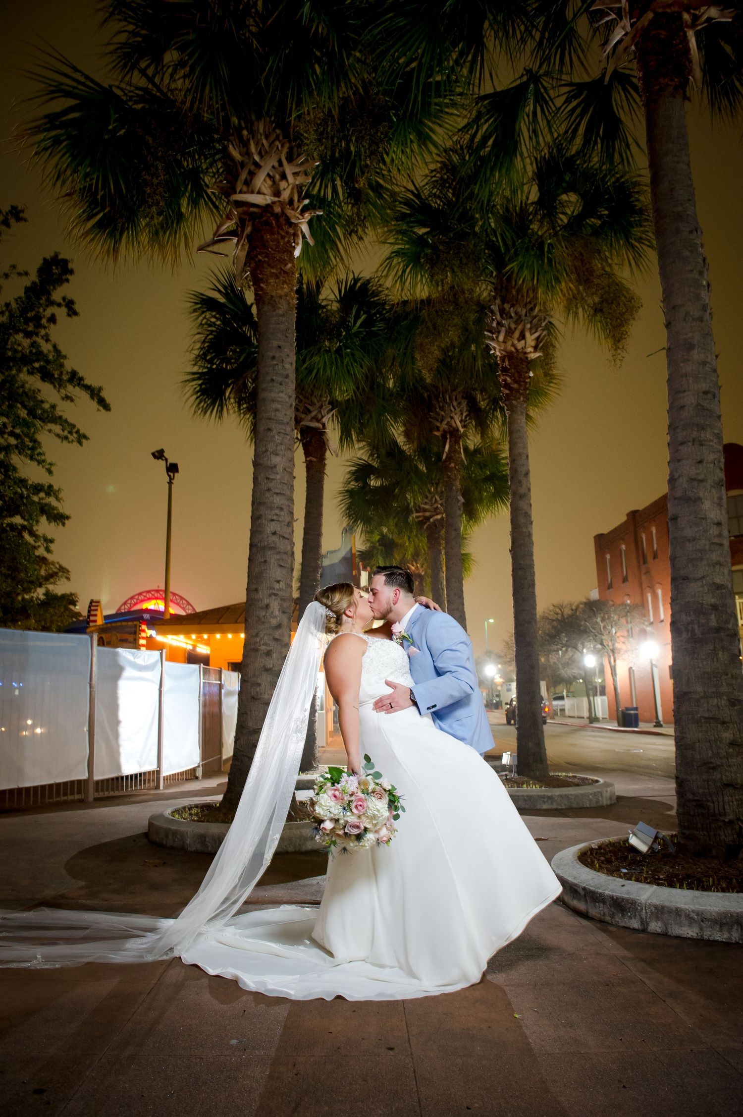 Romantic nighttime wedding photo under palm trees with dramatic lighting.