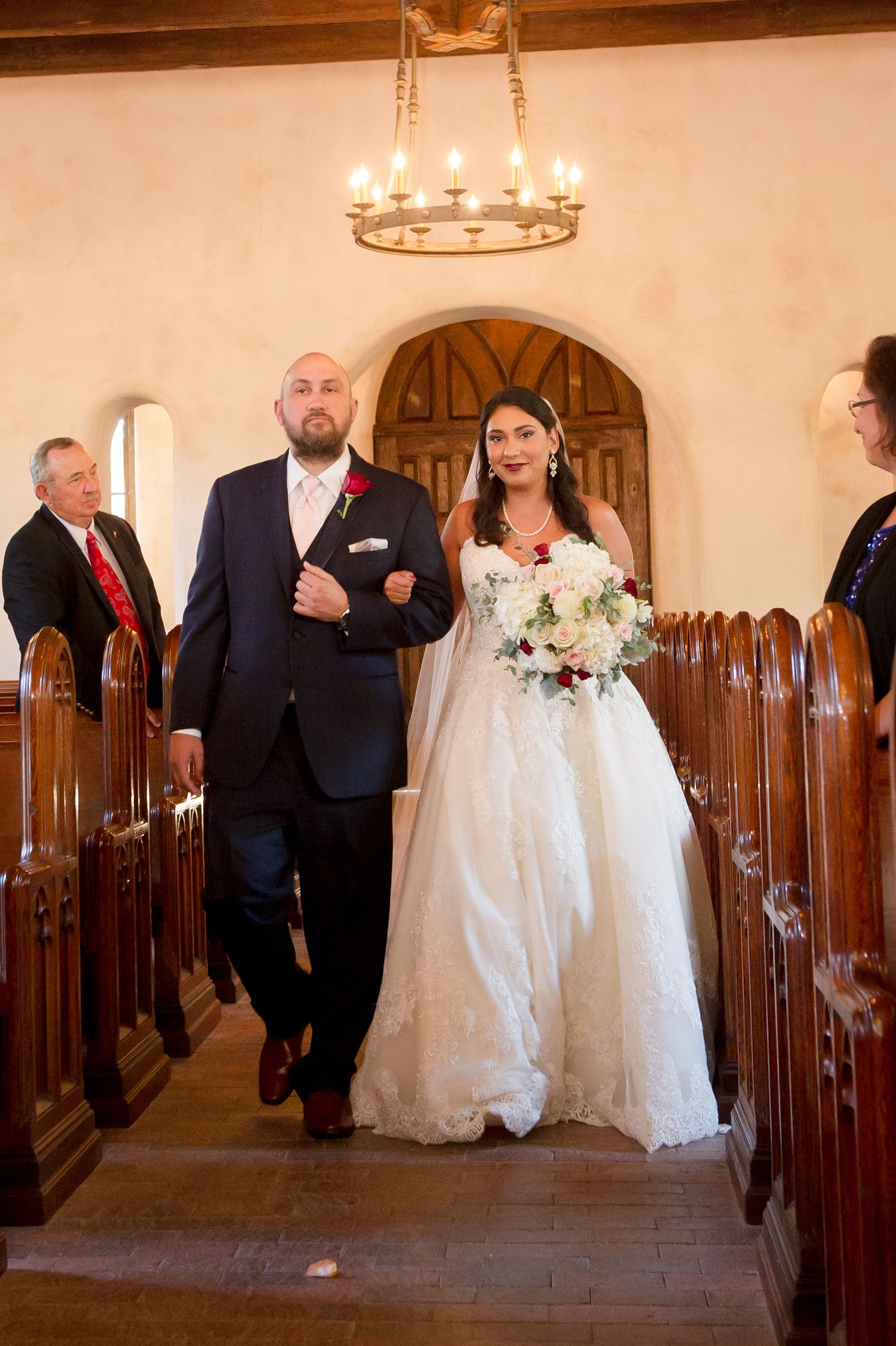 Wedding party members gather in a church corridor with wooden pews and warm lighting.