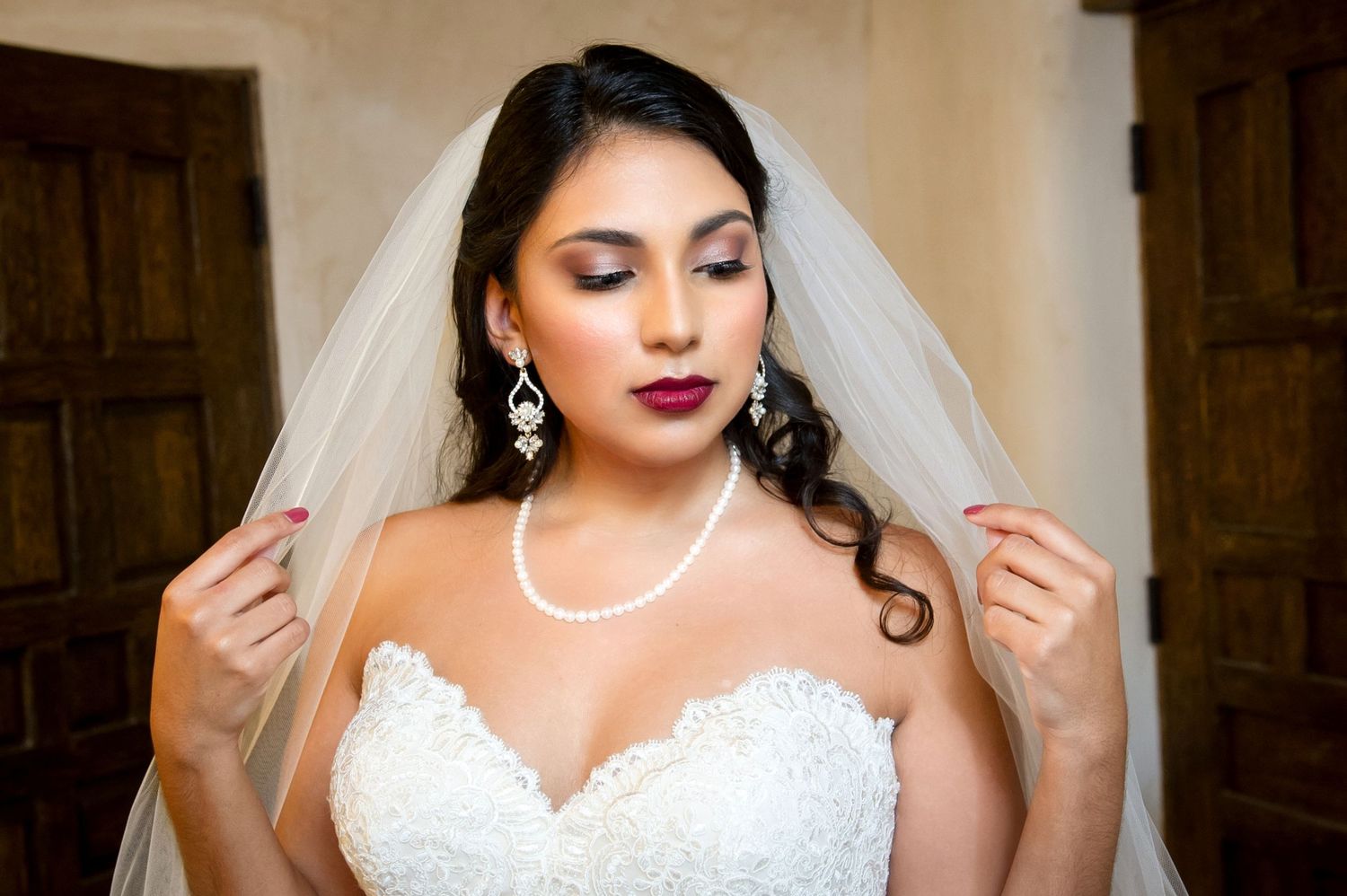 Bridal portrait featuring delicate veil, pearl necklace and crystal earrings with red lips.