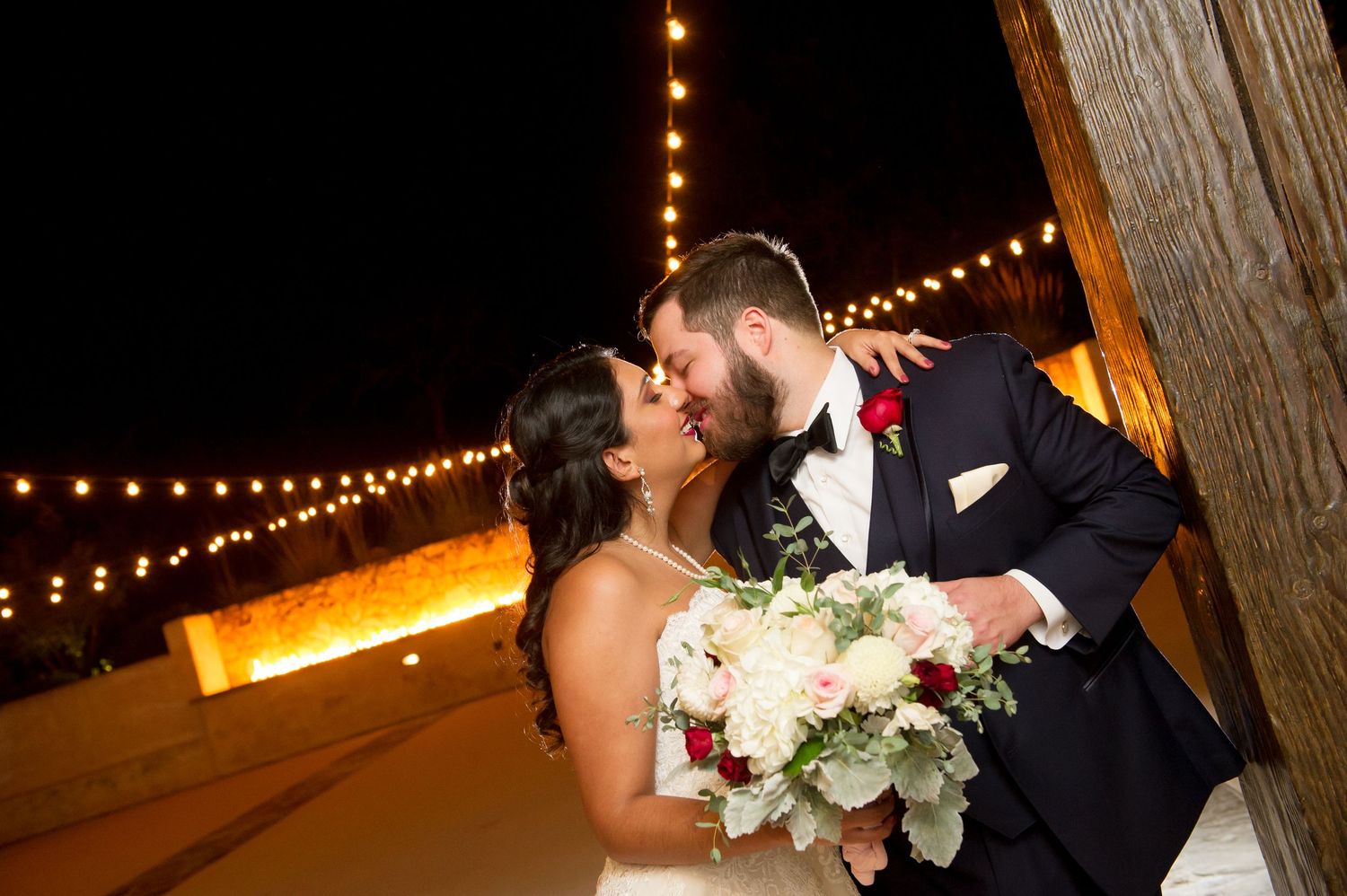 Evening wedding portraits under warm string lights create magical atmosphere.