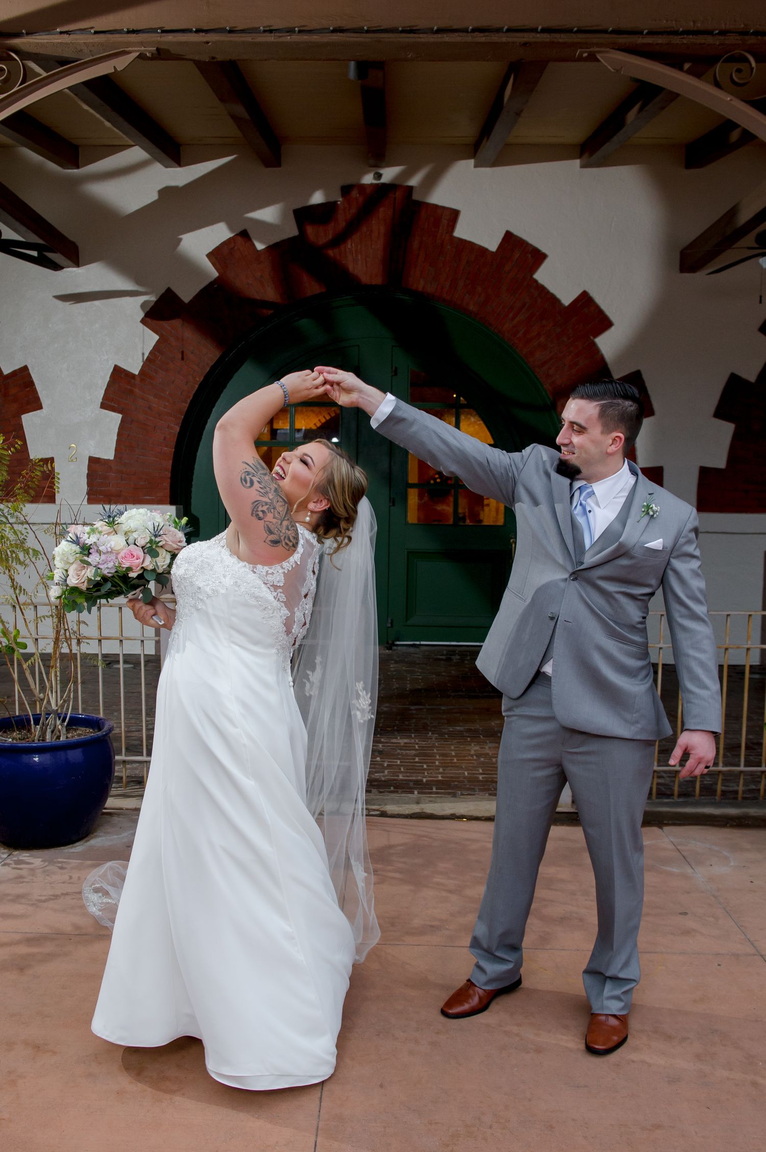 Wedding couple dances and twirls on terracotta tiled patio under wooden beams.