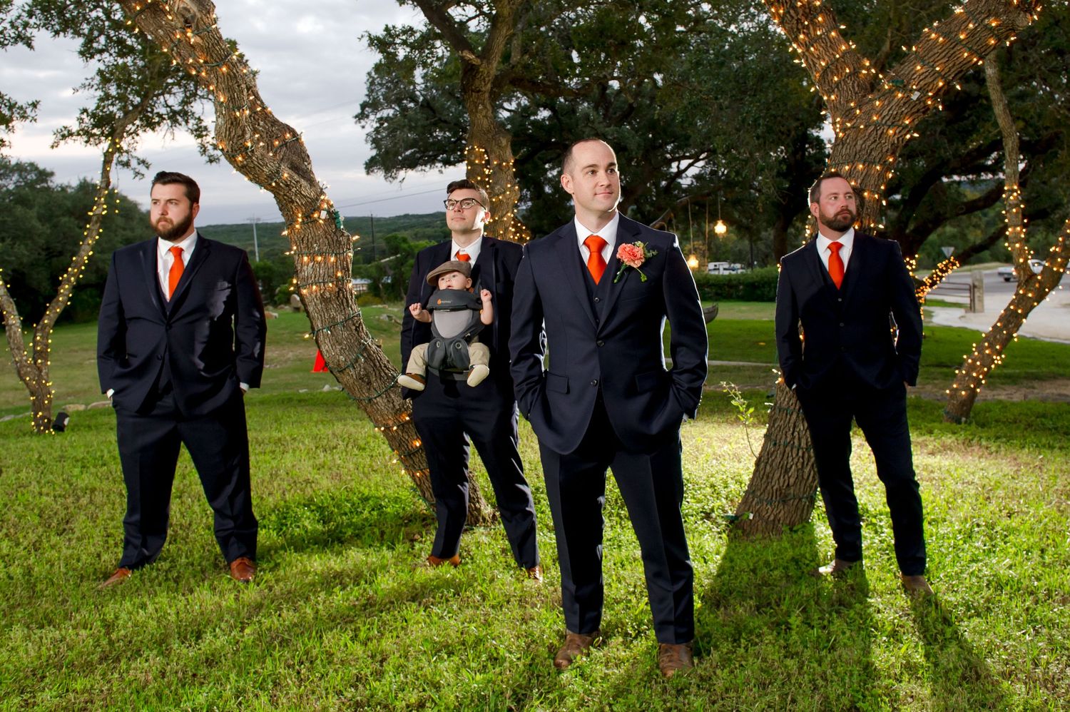 Wedding party in dark suits and dresses poses on grassy lawn during autumn.