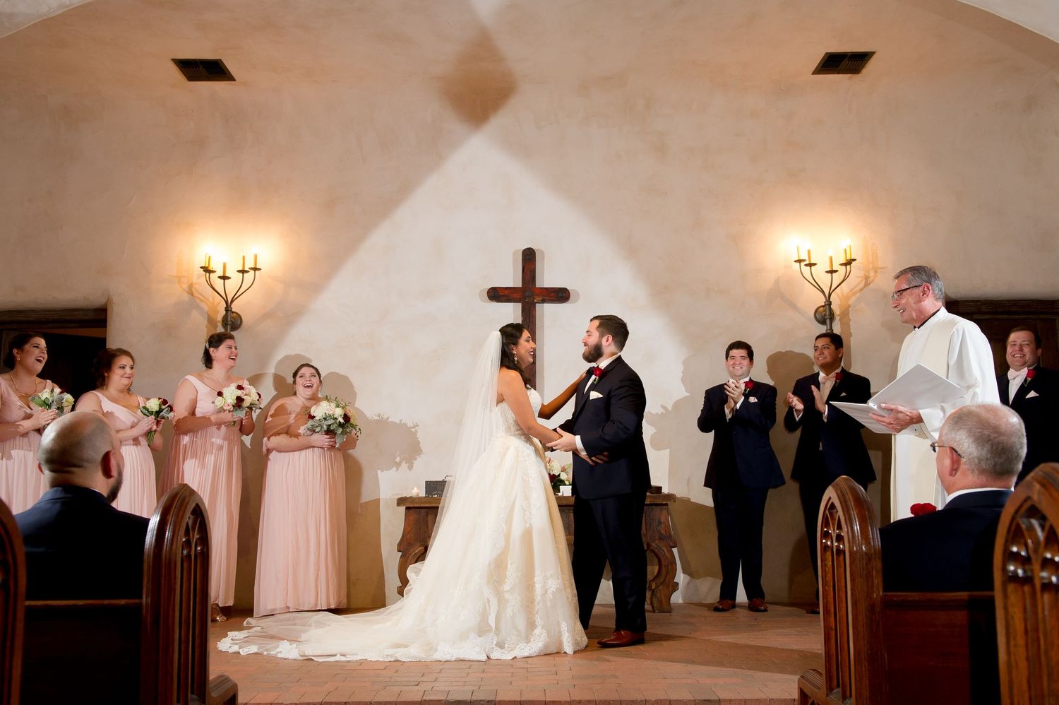 Wedding party gathered in church sanctuary during traditional ceremony with wooden pews and cross.