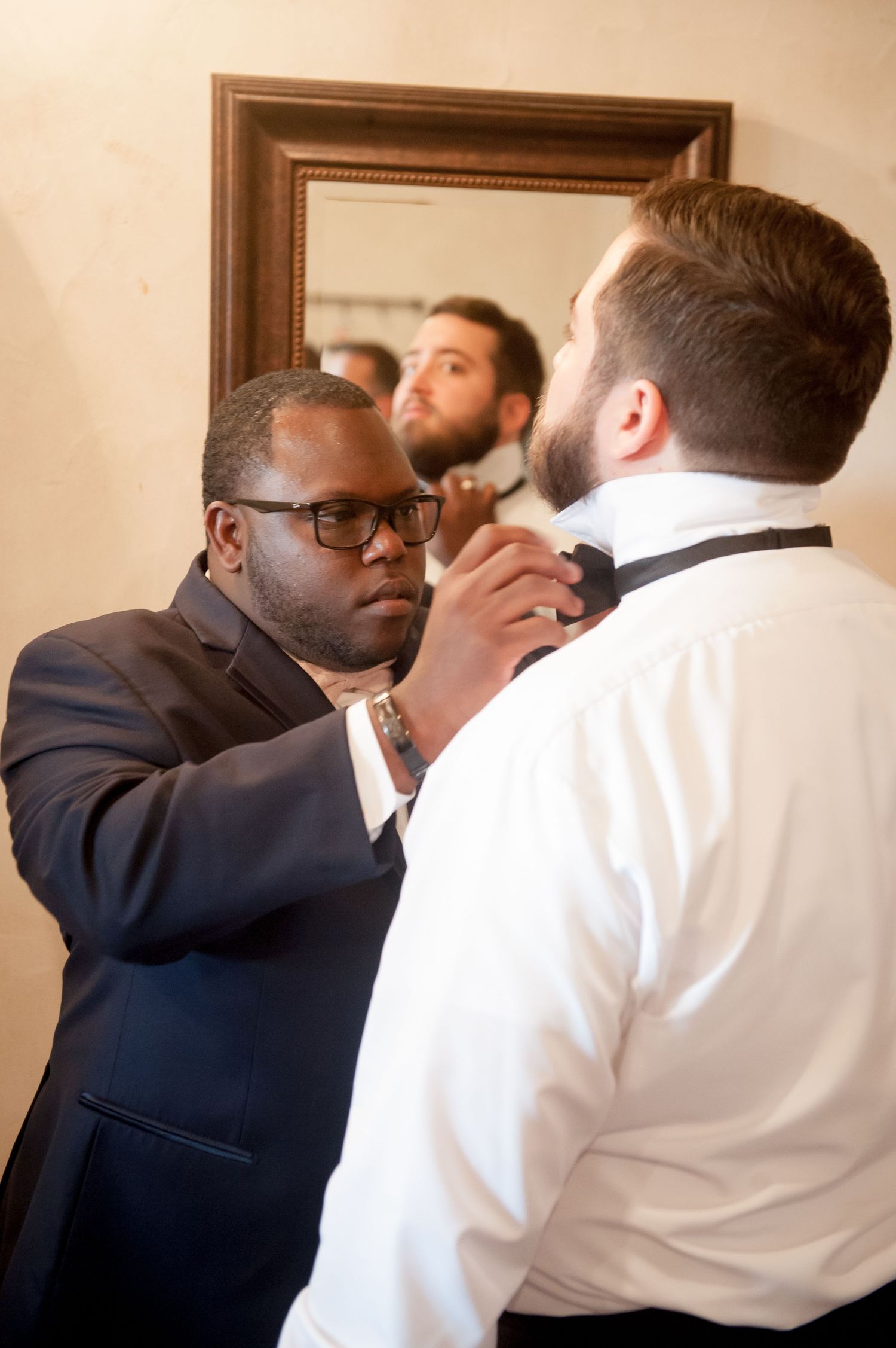 Groomsmen help adjust ties and collars during wedding day preparation.