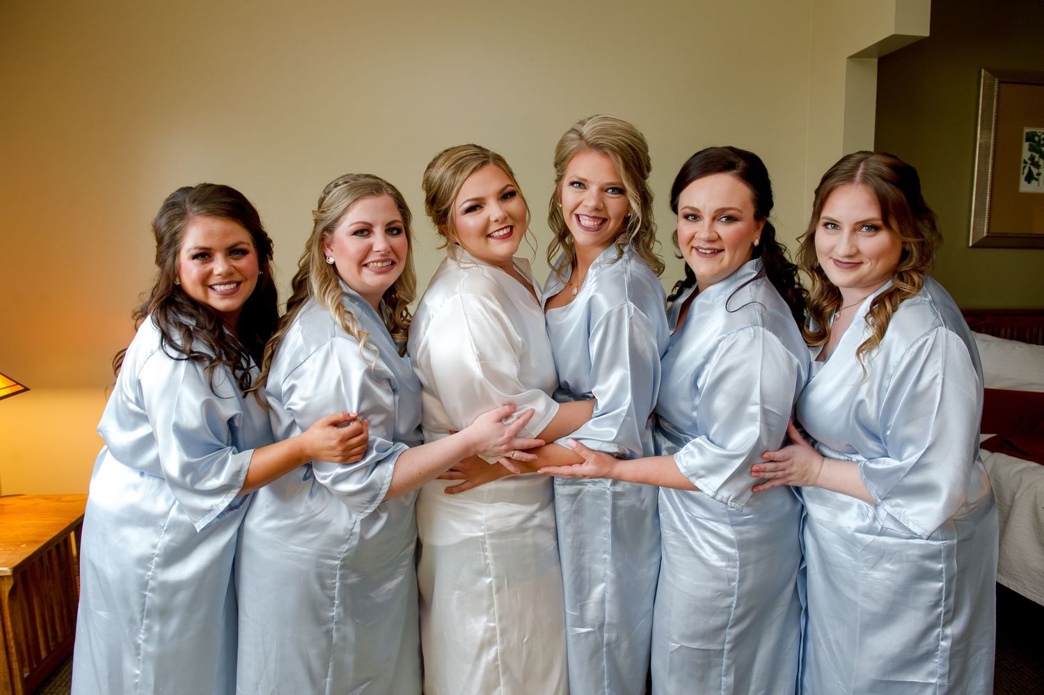 Group of bridesmaids in matching light blue robes sitting together on a couch.