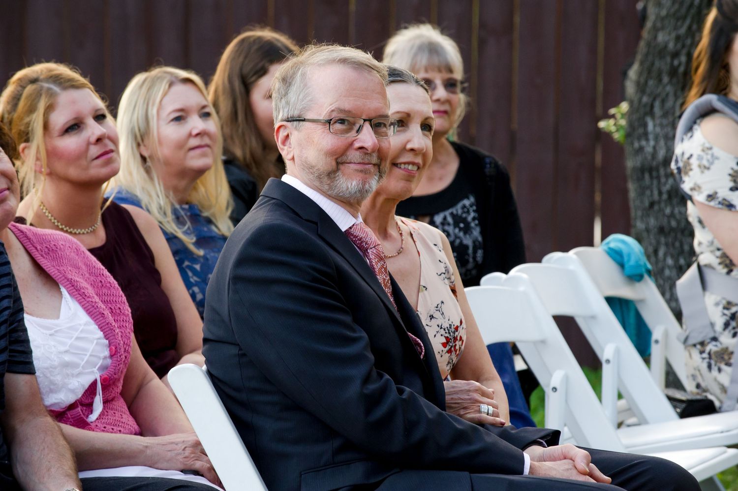 Wedding guests seated in rows during an indoor ceremony with dark curtains in background.