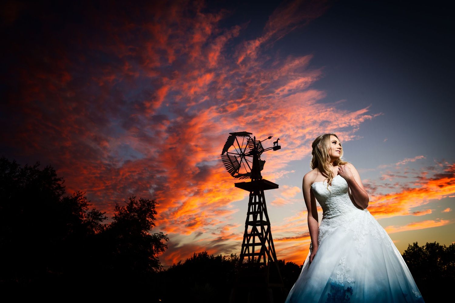 Wedding dress silhouette against dramatic red sunset sky with vintage windmill.