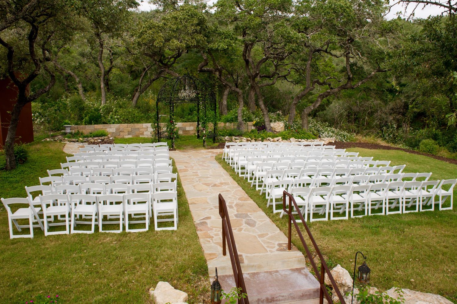 White wooden chairs arranged in rows for an outdoor wedding ceremony in a lush garden setting.