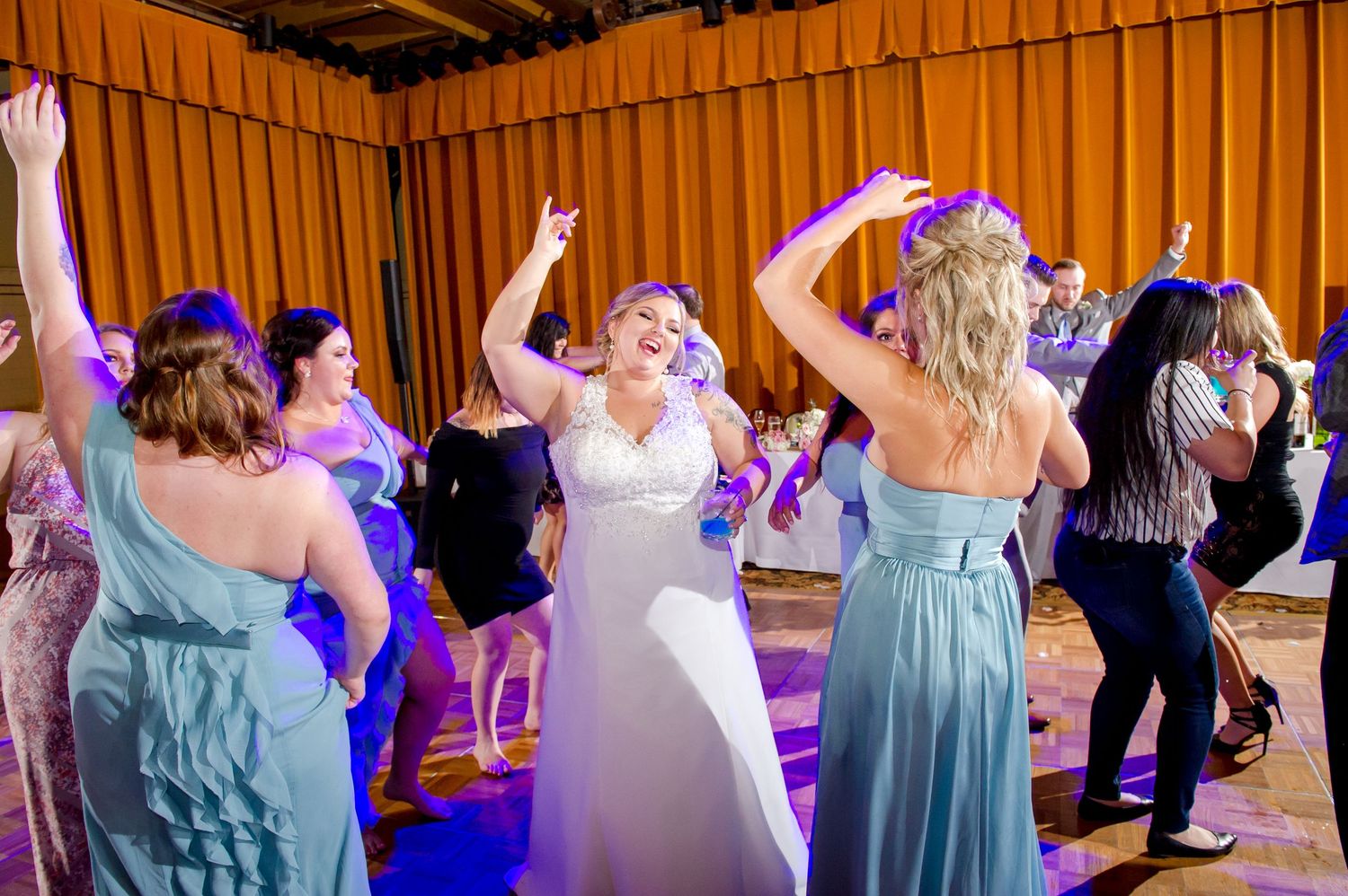 Wedding guests dancing in formal attire under decorative lighting at reception celebration.