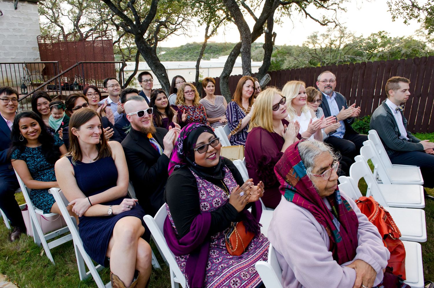 Wedding guests seated in white chairs watching outdoor ceremony.