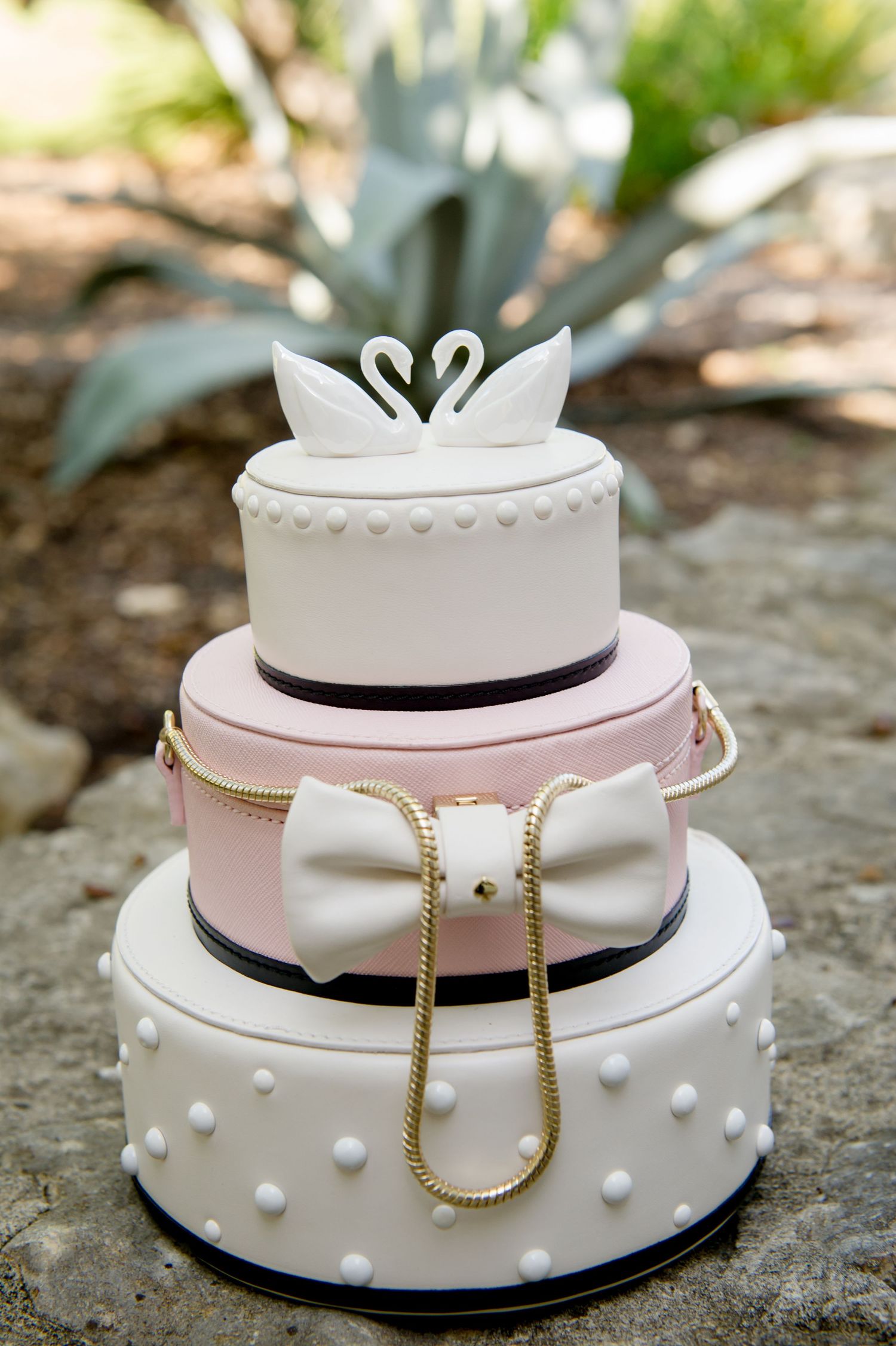 Three-tiered white and pink wedding cake decorated with pearls and swan topper.