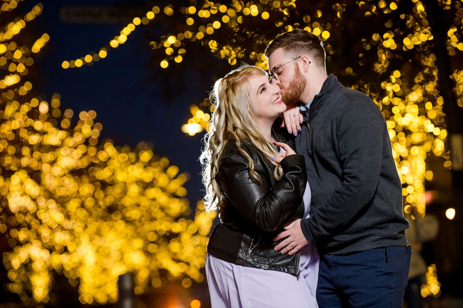 Newlyweds embrace under warm glowing string lights creating a magical evening atmosphere.