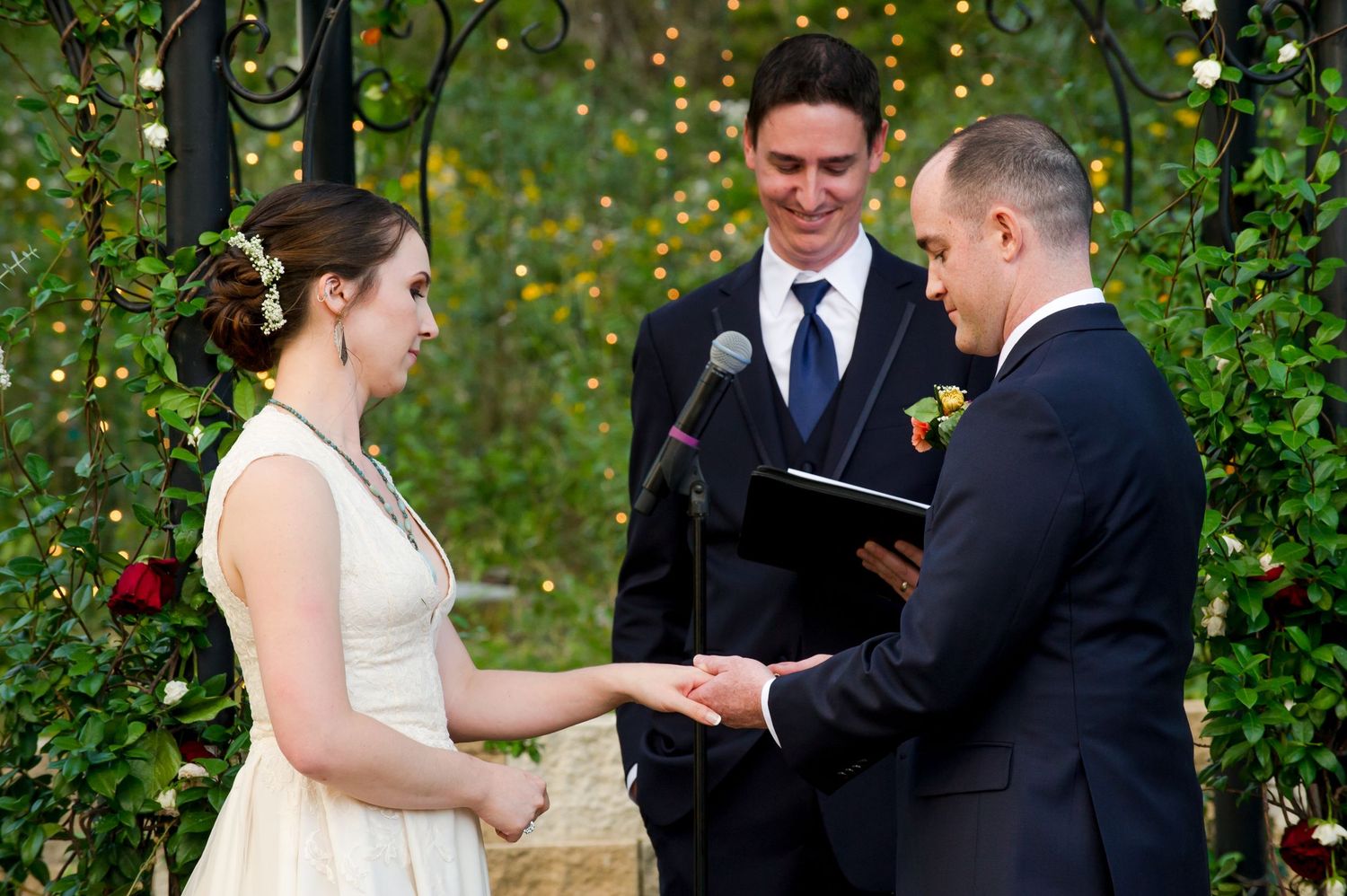 Outdoor wedding ceremony taking place in garden setting with twinkling lights and greenery.