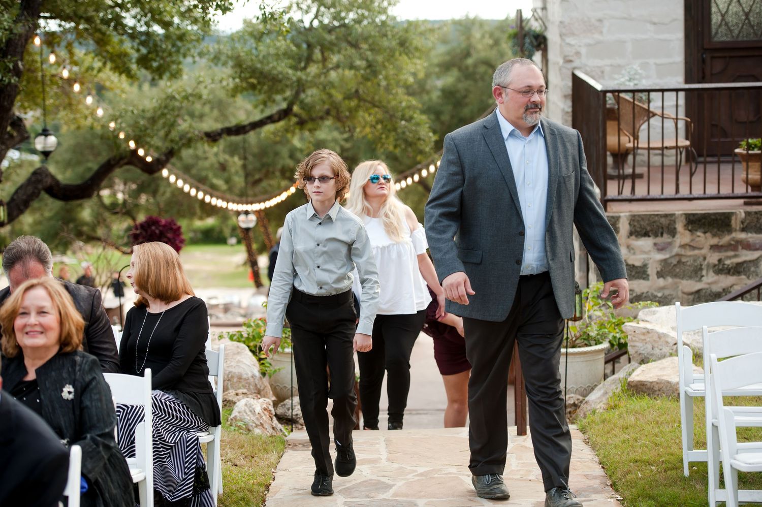 Wedding guests walk together on a stone pathway outside during an outdoor celebration.