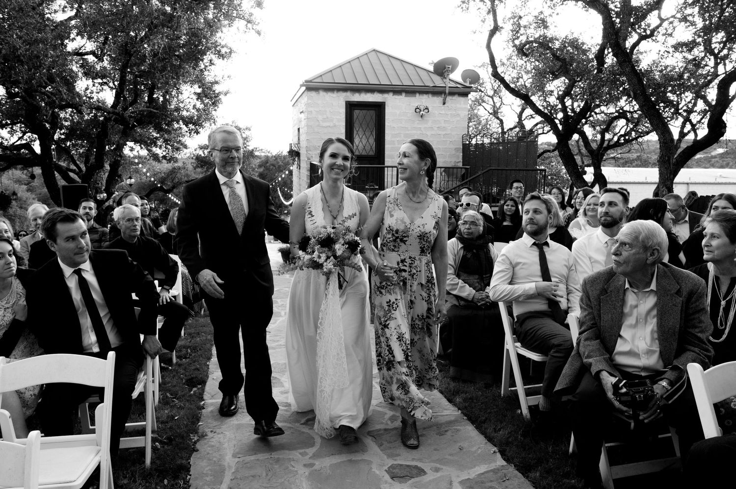 Wedding guests mingle and celebrate during an outdoor reception under trees.