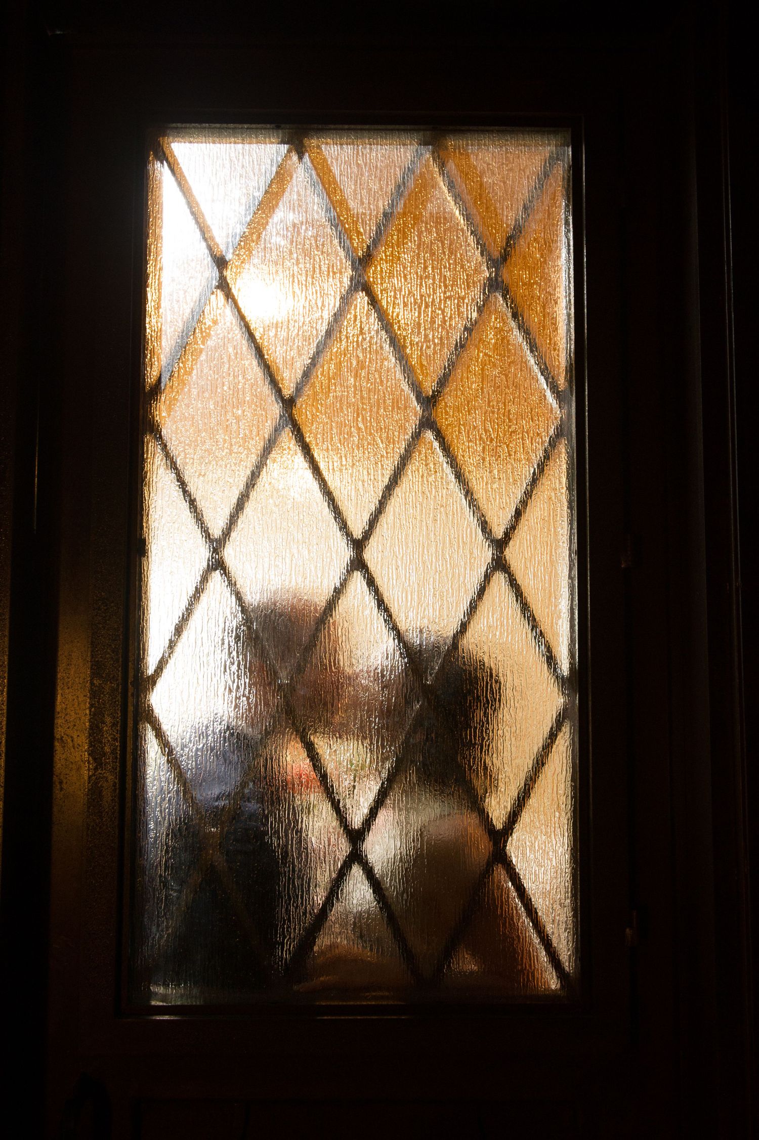 Silhouettes visible through frosted glass windows with diamond pattern create an artistic composition.
