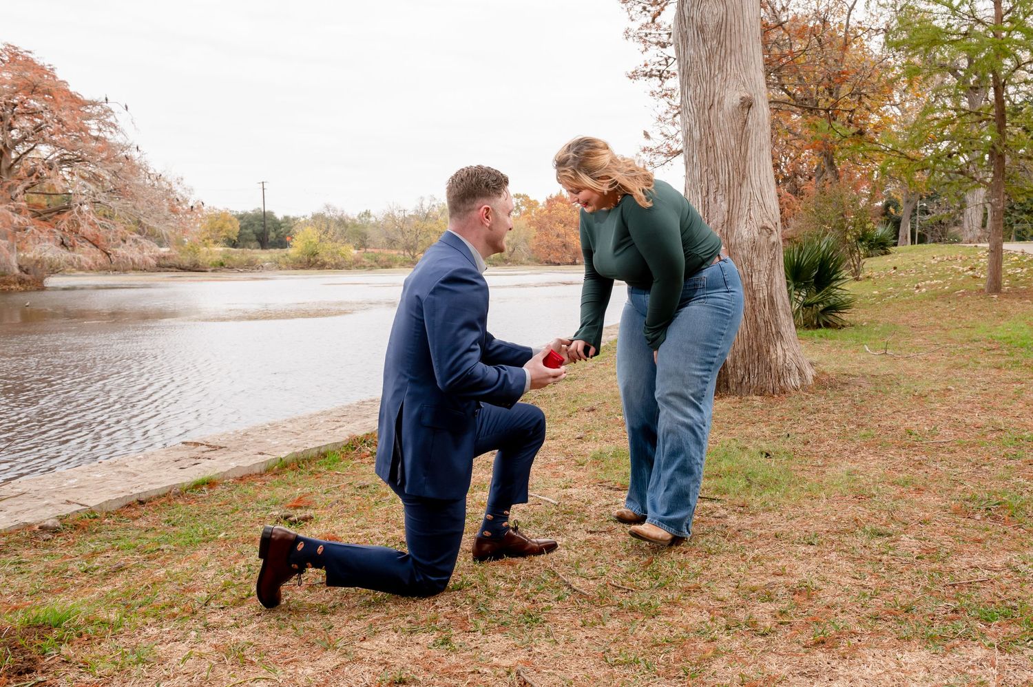 A marriage proposal scene unfolds by a scenic lake during autumn.