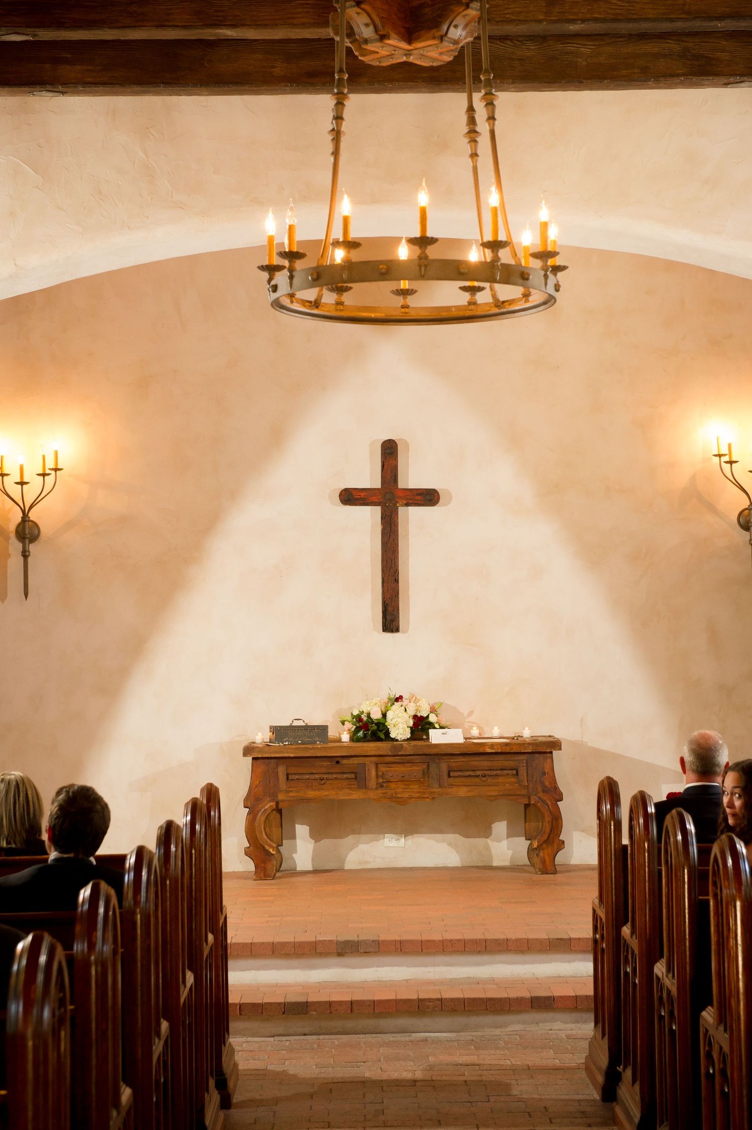 An elegant church interior with wooden pews and chandeliers illuminated for a wedding ceremony.