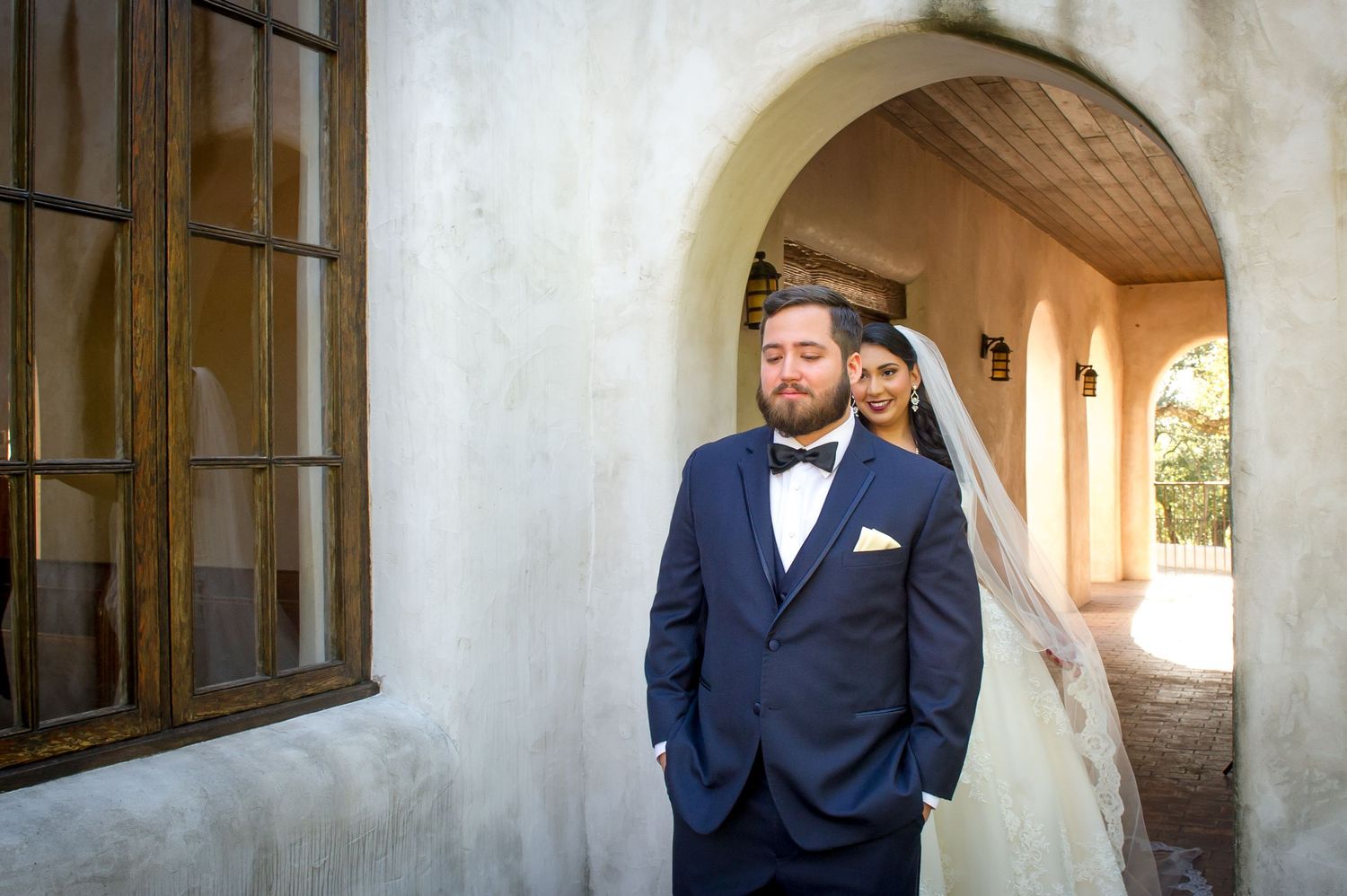 A couple shares their first look in an outdoor archway corridor with white stucco walls.