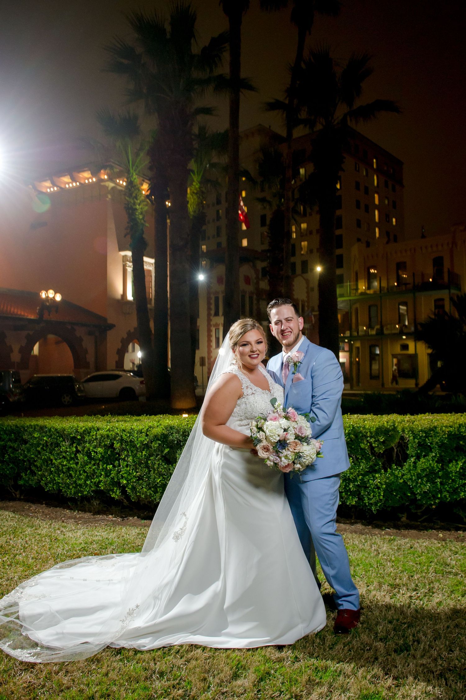 Nighttime wedding portrait on grass with twinkling lights in background.