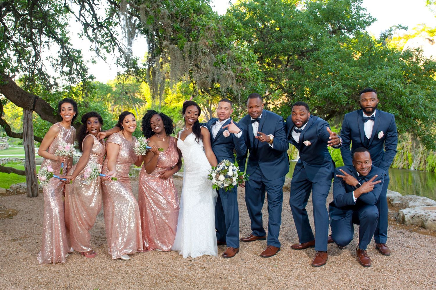 Wedding party in rose gold and navy attire poses together outdoors.