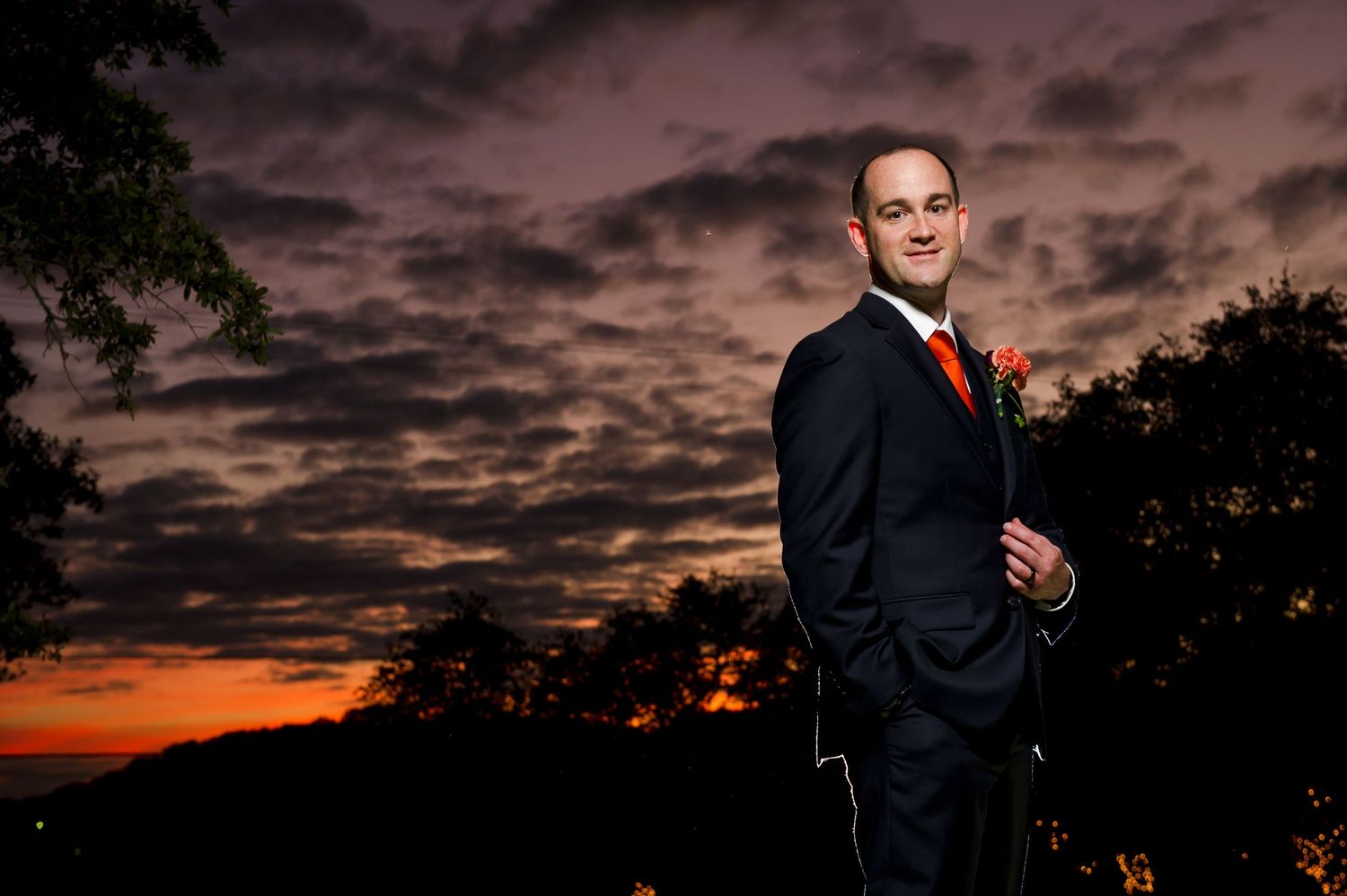 Silhouetted wedding couple embraces against vibrant orange and purple sunset sky.