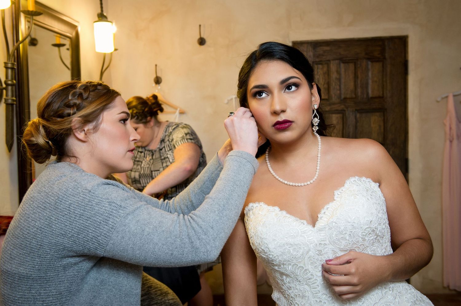 Final wedding preparation touches being applied in a room with vintage wooden doors and lighting.
