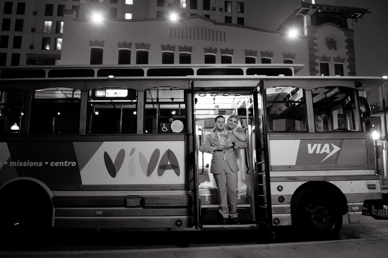 Black and white photo of a VIA transit bus at night with open doors at a bus stop.