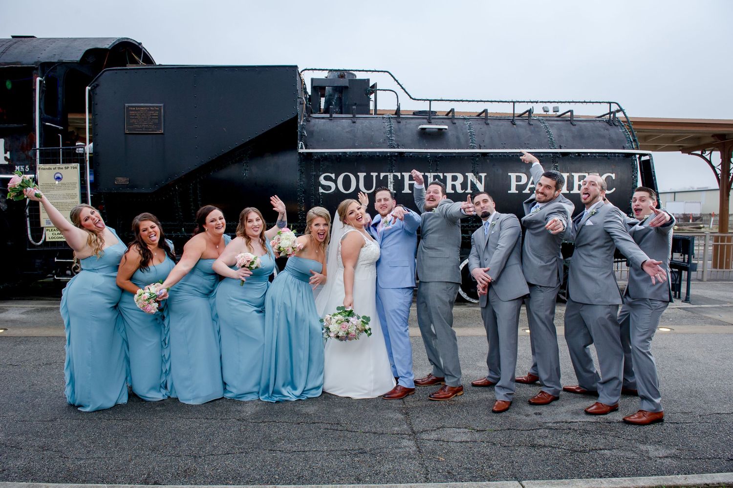 Wedding group creates fun photo lineup against Southern Pacific train backdrop.