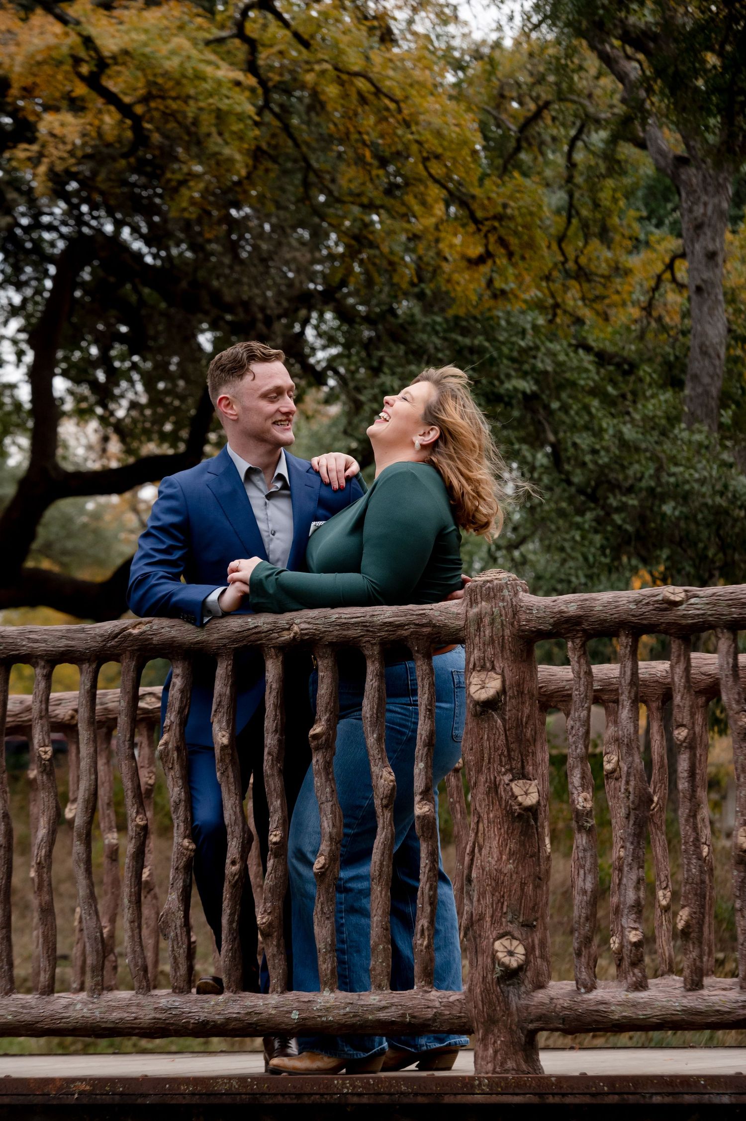 A couple shares a joyful moment on a rustic wooden bridge during autumn.