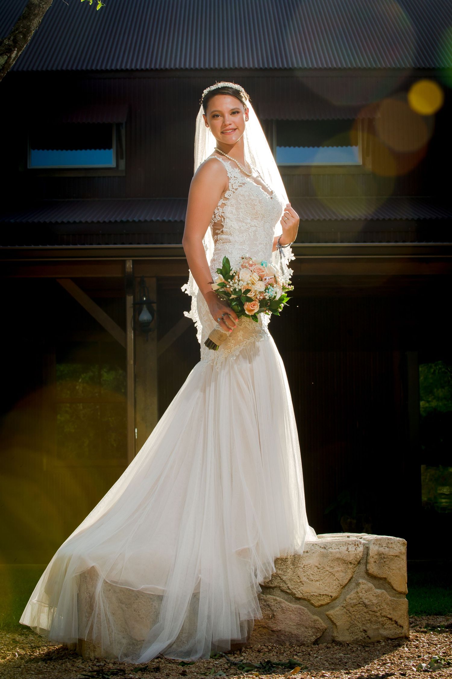 A bride in a tulle ballgown poses against a dark background with sunlit edges.