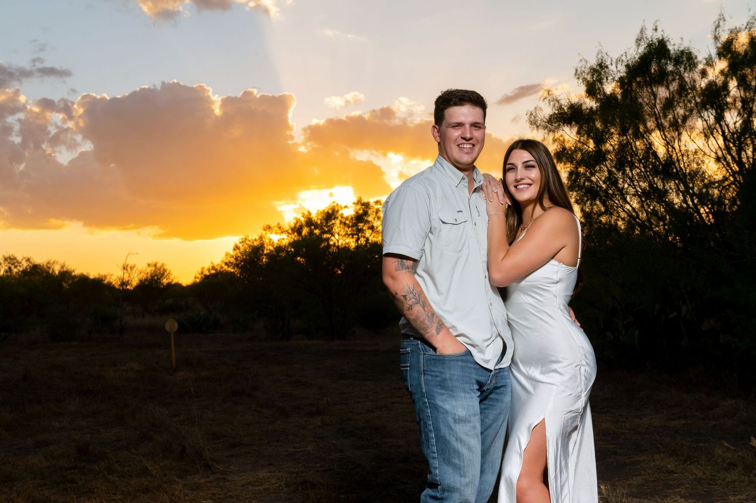 Couple posing against dramatic orange sunset sky in elegant attire.