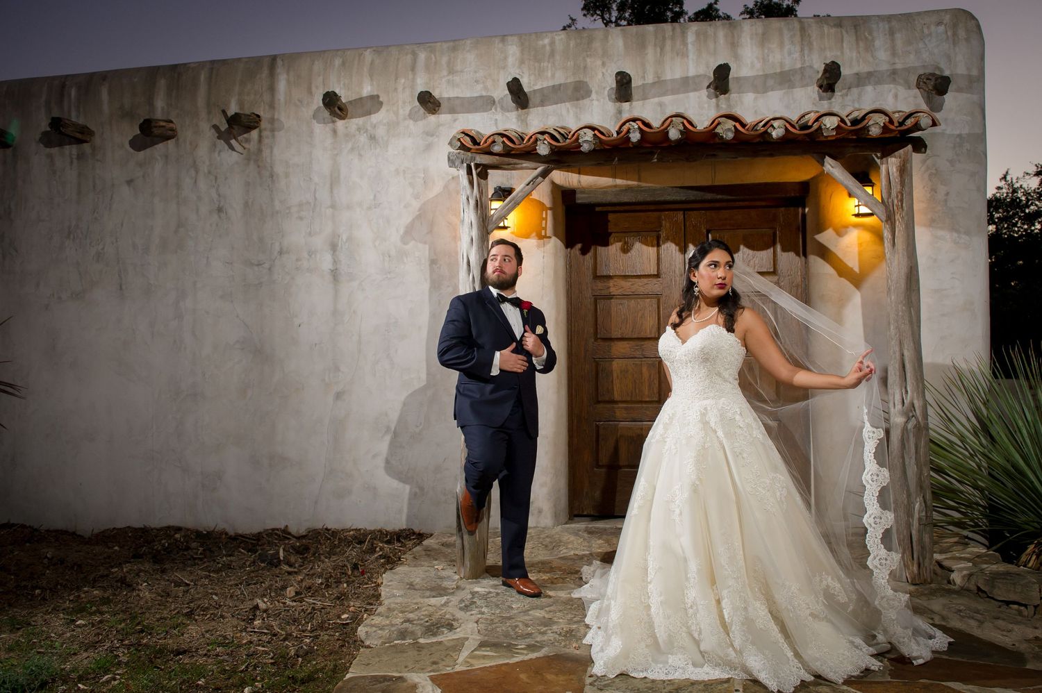 A romantic wedding moment captured against rustic stone walls and Spanish-style architecture.