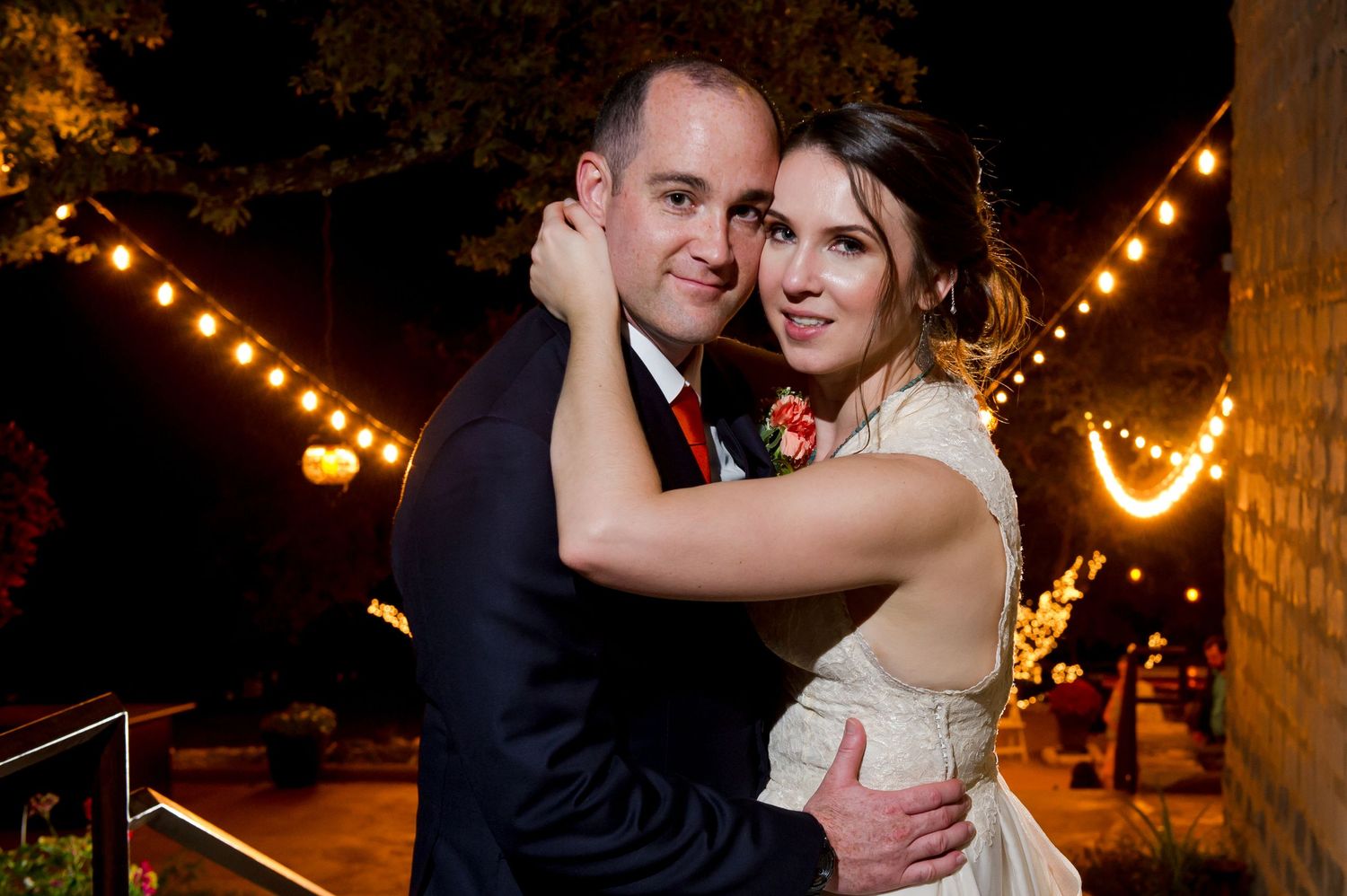 A couple shares a romantic dance under twinkling string lights at an outdoor evening wedding reception.