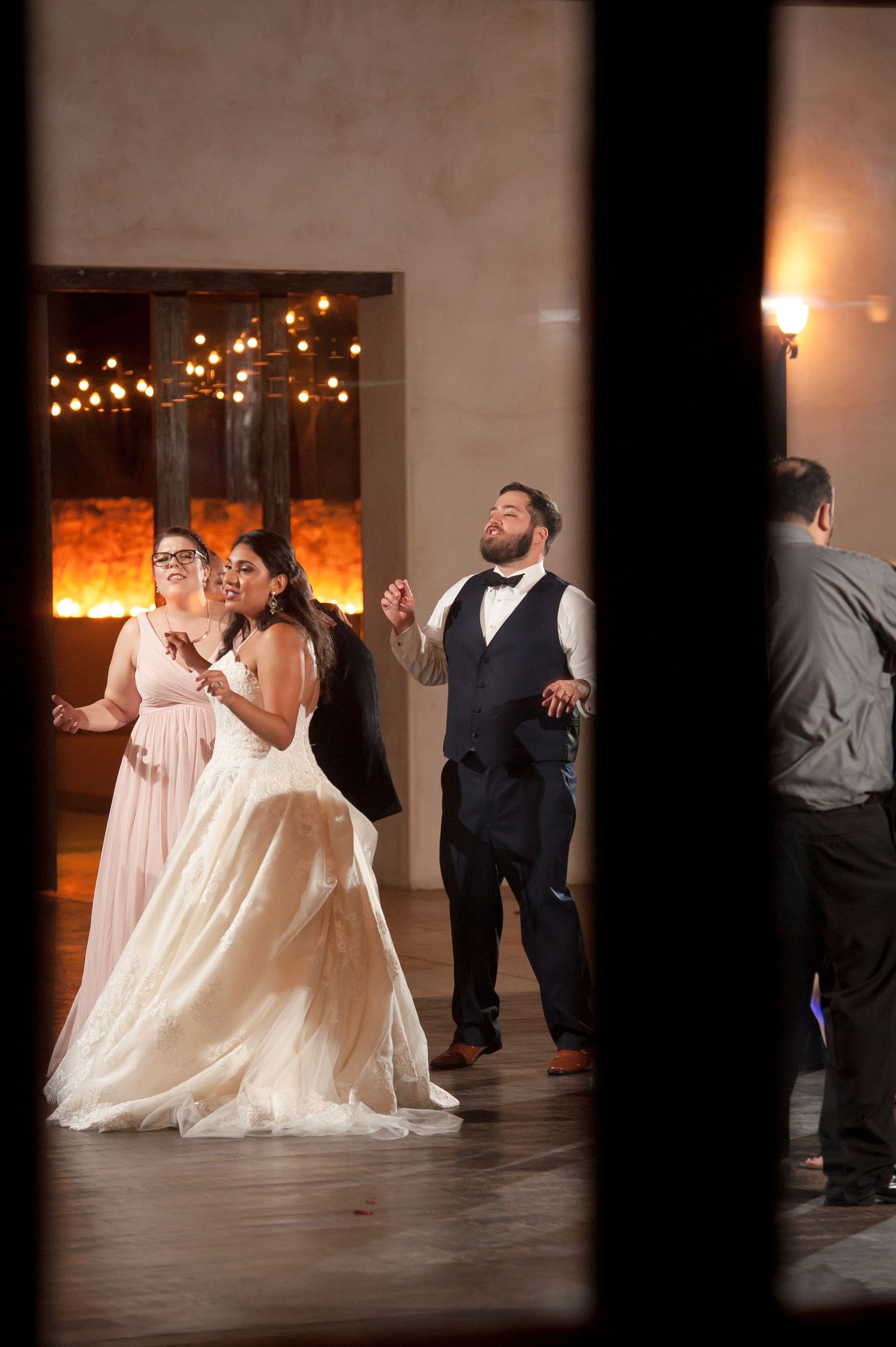 Wedding party members dance and twirl in formal attire on a wooden dance floor.