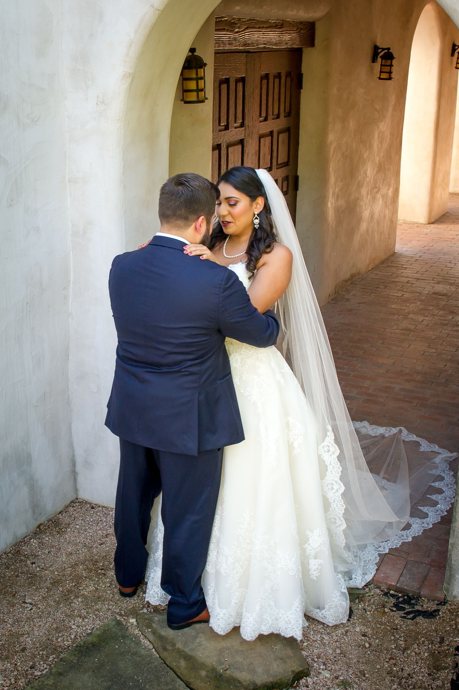 A bride and groom have their first look in a mission-style covered walkway.