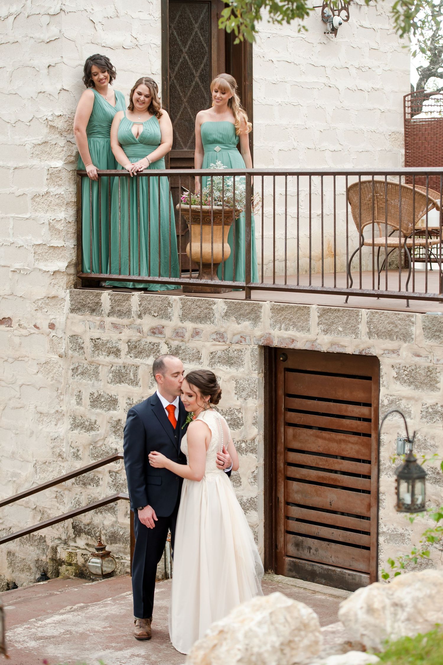 Wedding party in teal bridesmaid dresses poses on a rustic stone staircase at an elegant venue.