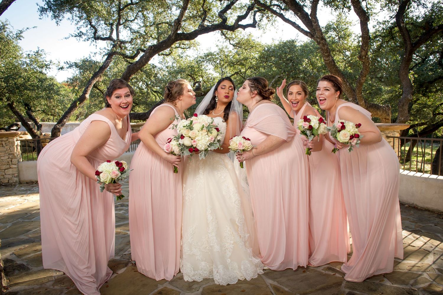 Bridesmaids in blush pink dresses pose together outdoors for wedding photos.